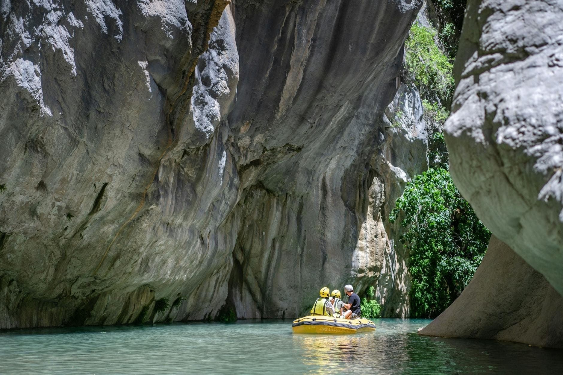Eine kleine Gruppe beim Rafting durch die beeindruckenden Felswände und das türkisfarbene Wasser des Köprülü Canyons, umgeben von üppigem Grün und Felsformationen.