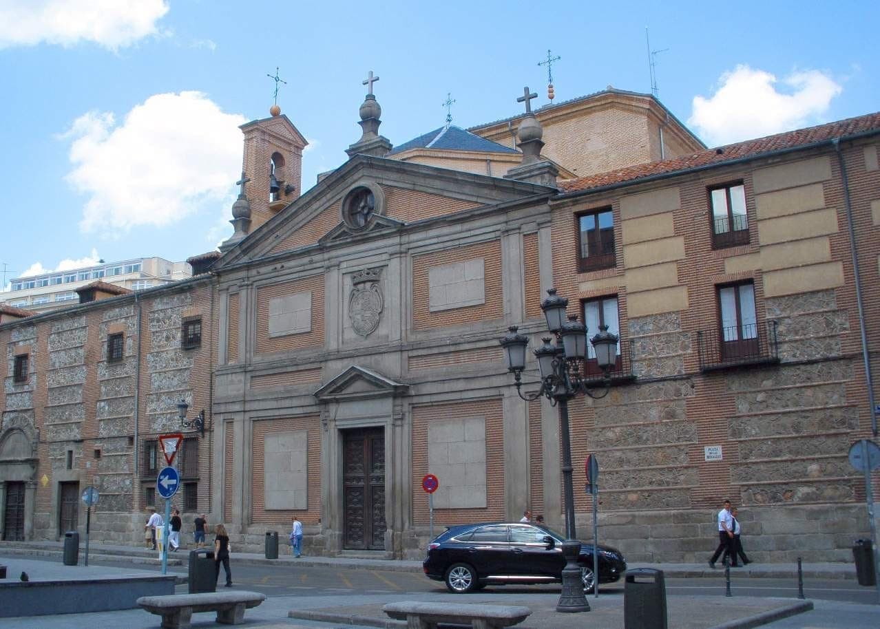 Фасад Real Monasterio de las Descalzas Reales в Мадриде: кирпичный экстерьер, богатая каменная отделка и прохожие на улице.