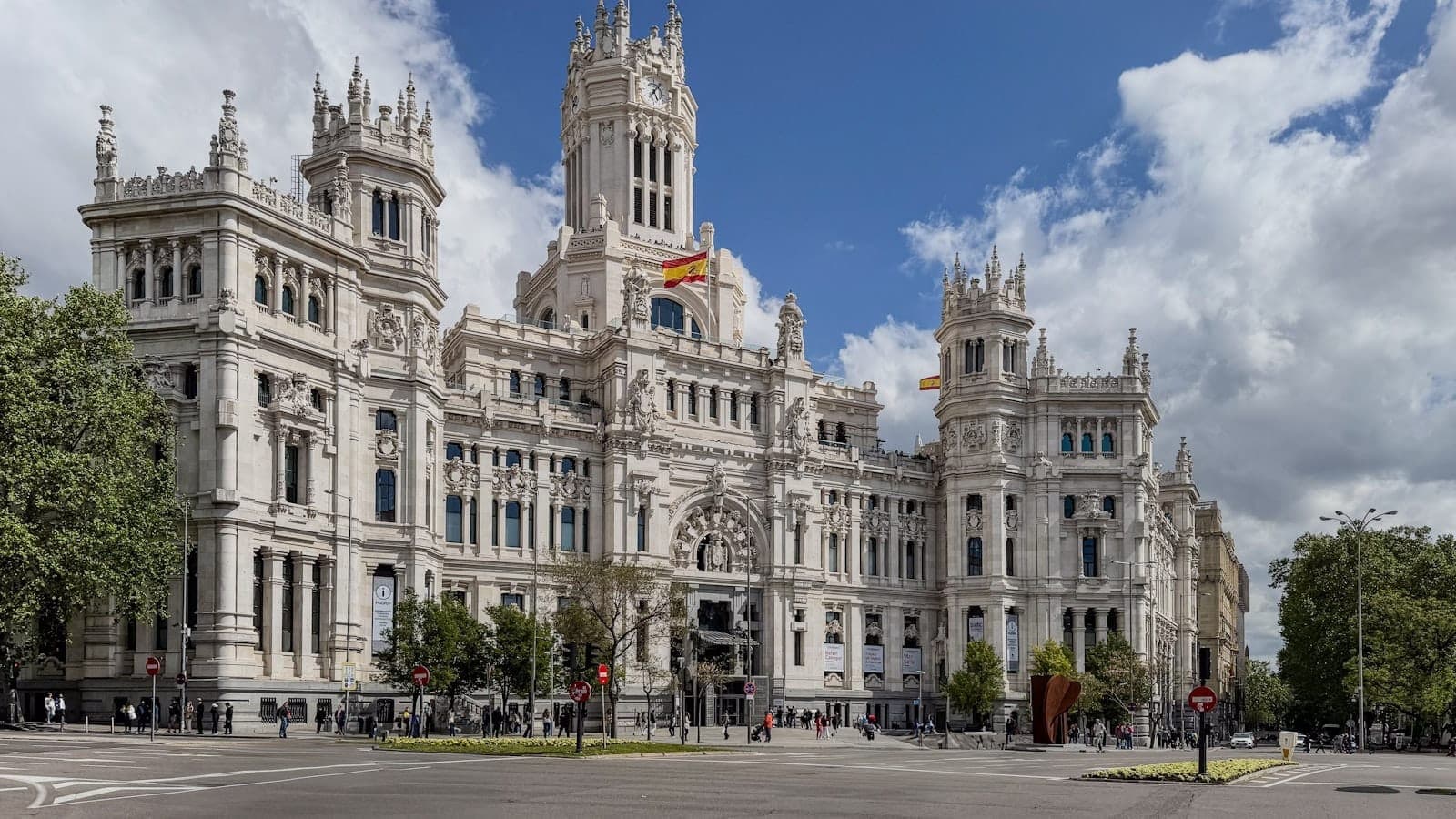 มุมกว้างของ Palacio de Cibeles กับต้นไม้ ธงชาติสเปน และท้องฟ้าแจ่มใส เป็นภาพแทนบรรยากาศย่านเรติโรในมาดริด