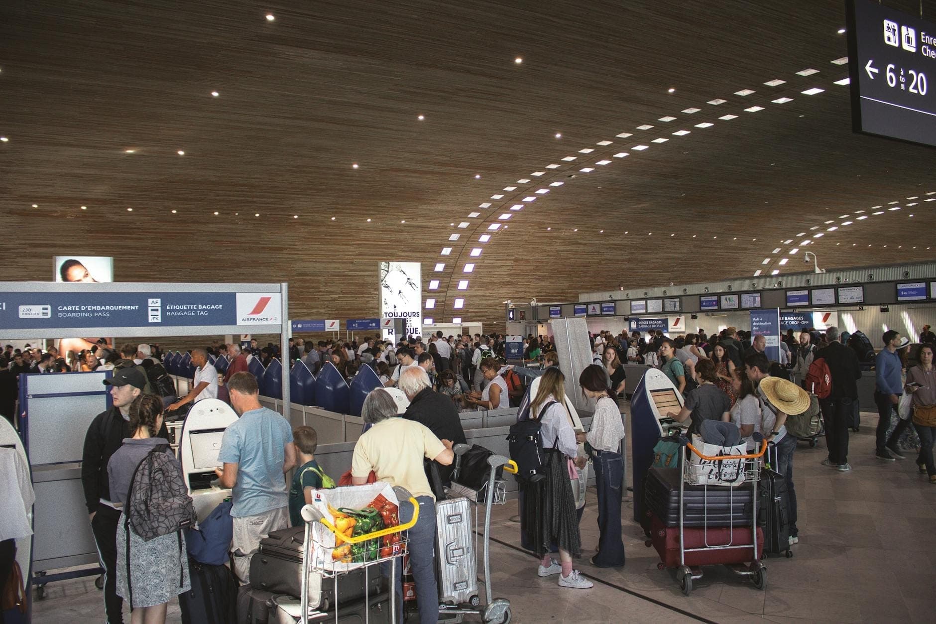 Zone d'enregistrement animée d'un aéroport avec des foules de voyageurs et des chariots à bagages dans un terminal moderne avec un plafond en bois.