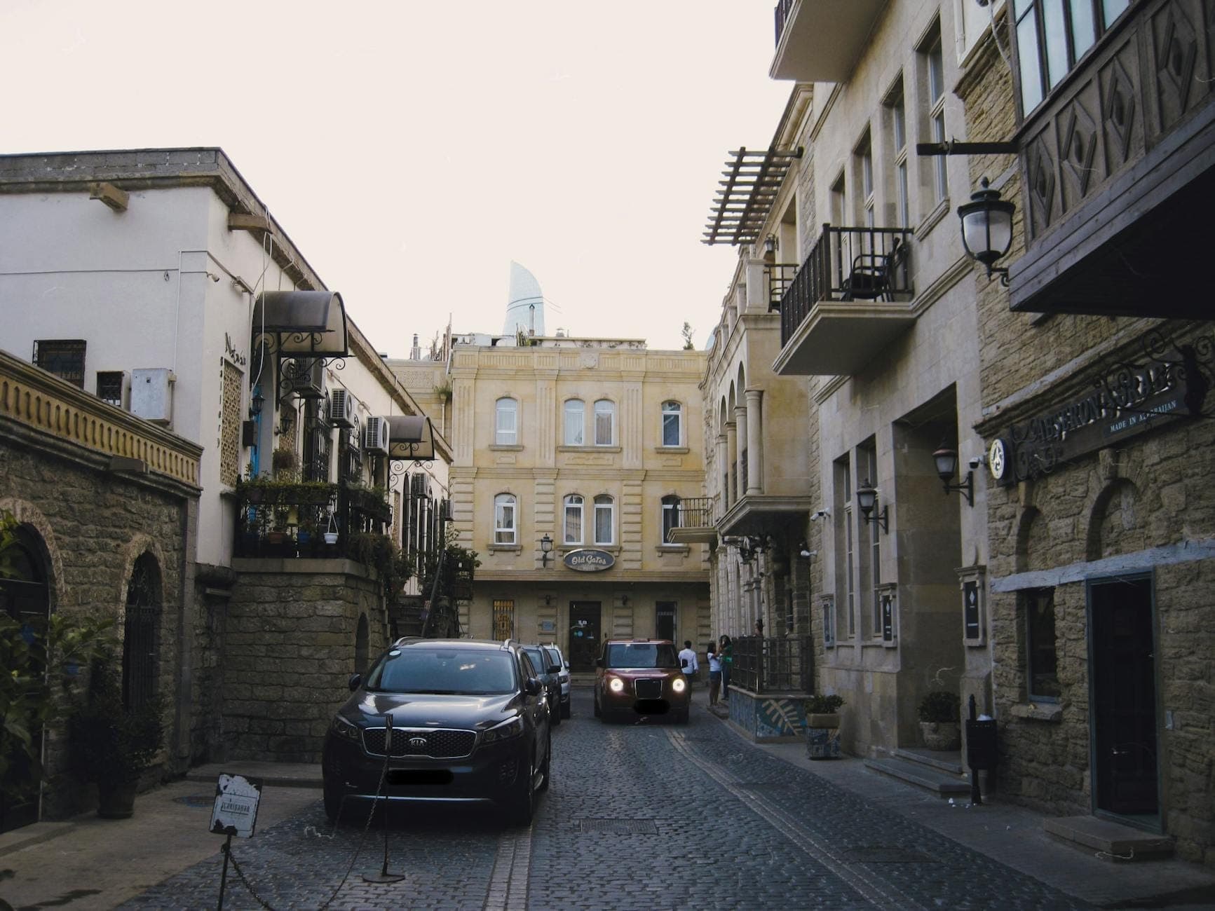Cars parked along a narrow cobblestone street lined with historic Mediterranean-style buildings in a town setting.