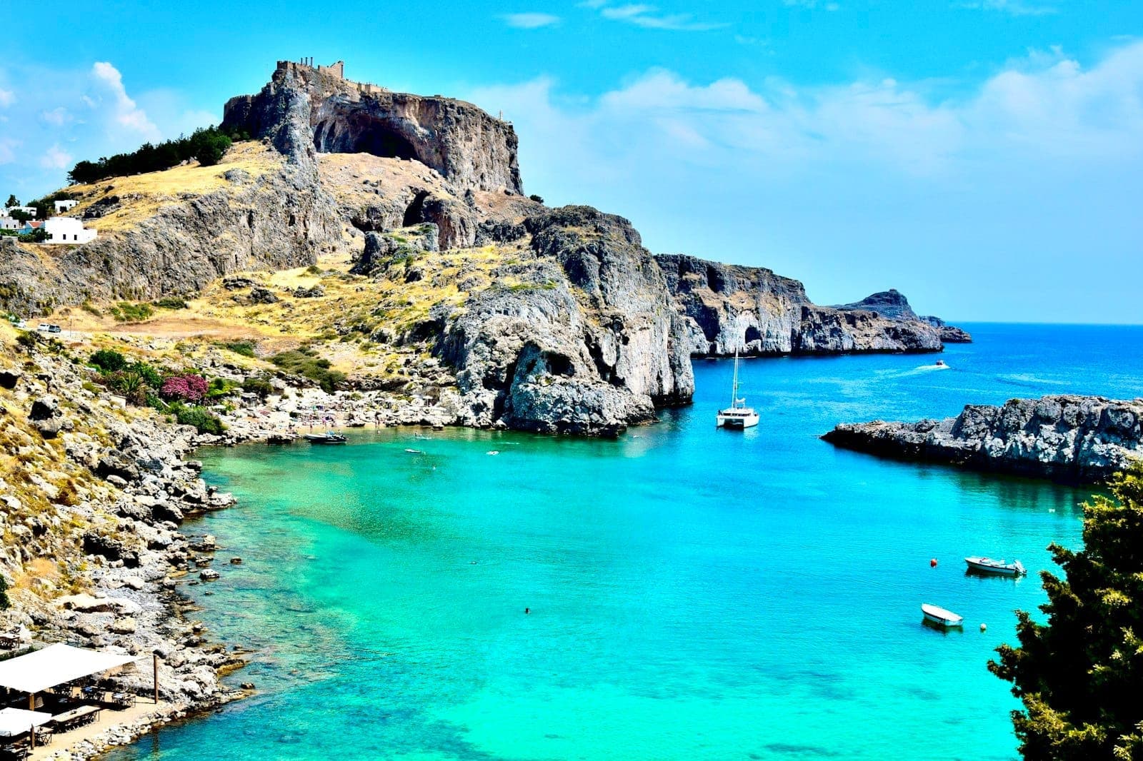 Eau turquoise claire et littoral rocheux avec des bateaux ancrés sous l'ancienne Acropole de Lindos à Rhodes lors d'un après-midi ensoleillé.