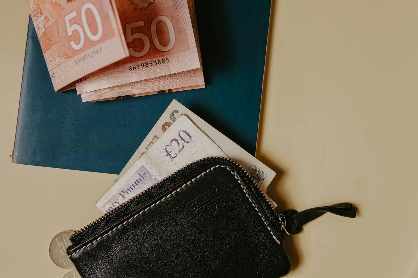 Portefeuille et diverses devises dont des billets en euros et en livres sterling posés sur une table, évoquant la gestion d'un budget voyage à l'étranger.