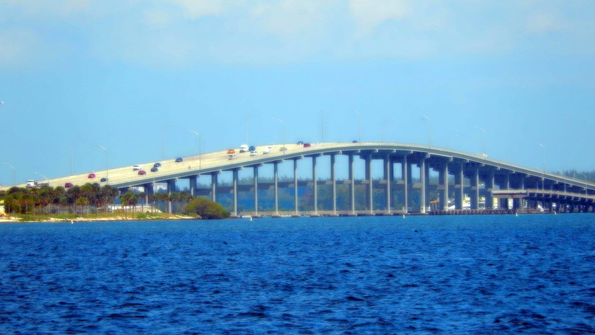 Rickenbacker Causeway spanning Biscayne Bay with vehicles crossing, surrounded by blue water and palm trees under a clear sky.