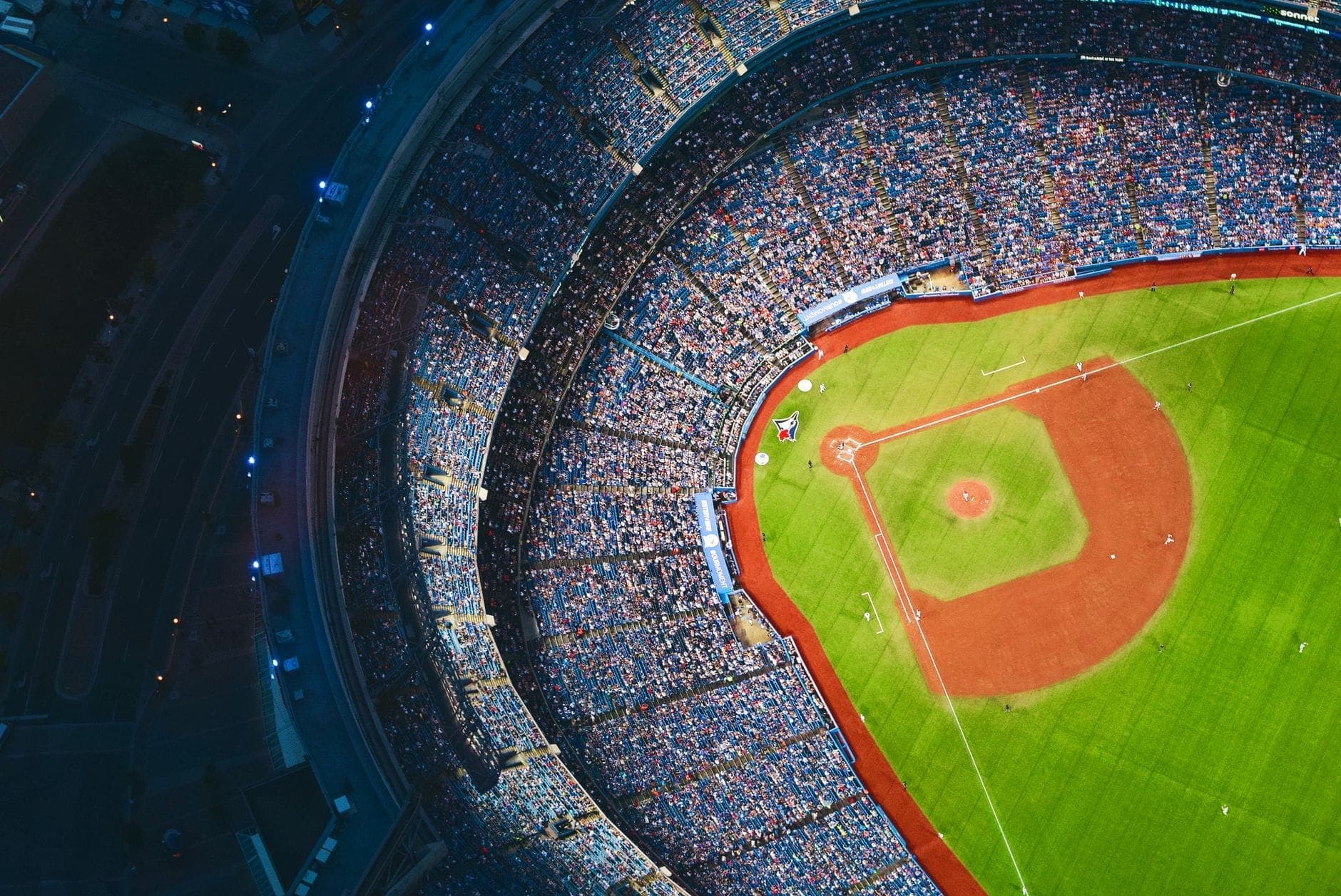 Vista aerea del Rogers Centre gremito di tifosi, con il brillante campo da baseball verde, i vivaci sedili dello stadio e le strade circostanti di Toronto di notte.