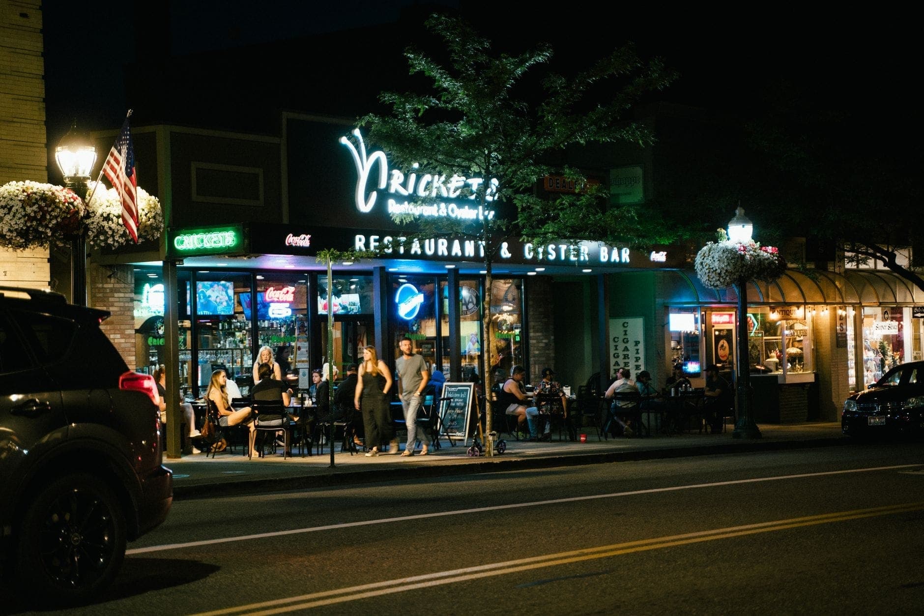 Vista notturna di persone che cenano all'aperto al Cricket's Restaurant & Oyster Bar a Nashville, con insegne al neon luminose e un'atmosfera rilassata e accogliente.
