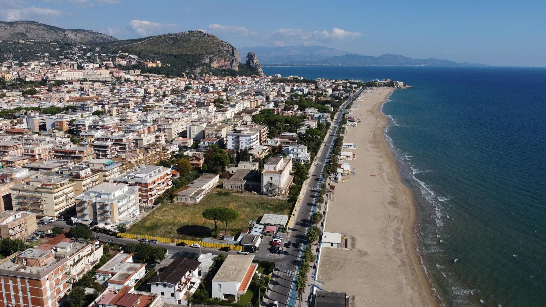 Cảnh nhìn từ trên cao của một thị trấn biển Italy thơ mộng với bờ cát dài, làn nước xanh lấp lánh và những ngọn đồi ở phía sau.