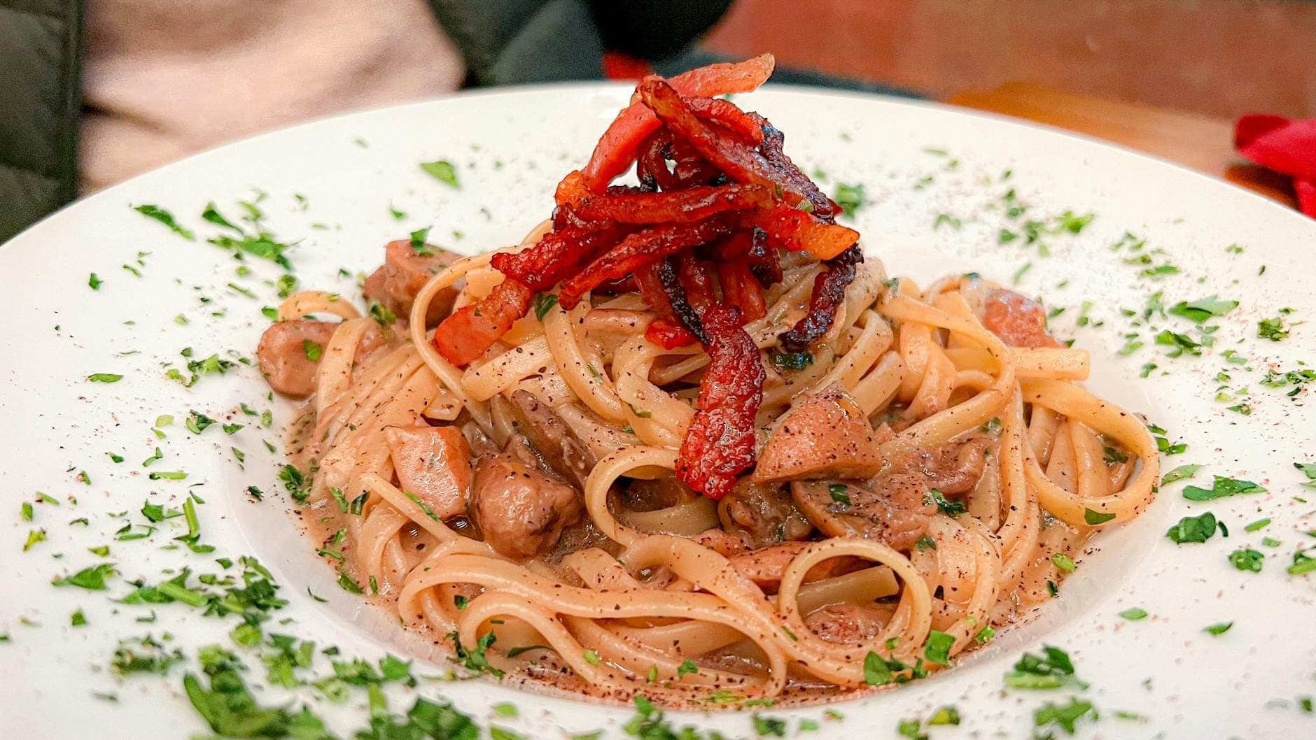 Um prato de massa com guanciale e salsa, provavelmente um prato romano como a carbonara ou a amatriciana, servido numa mesa ao ar livre.