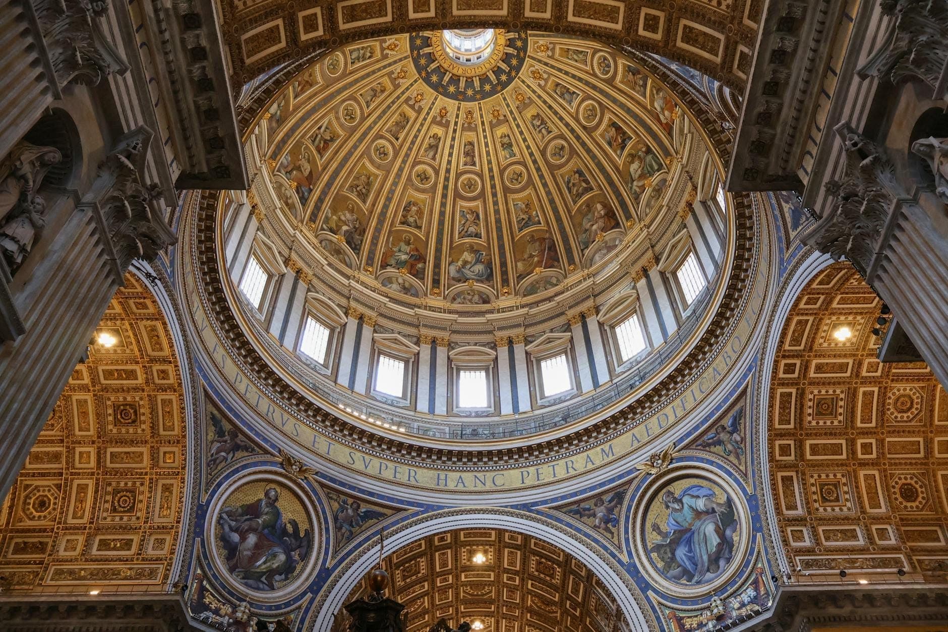 Vue intérieure large de la coupole de la Basilique Saint-Pierre et de son architecture ornée, avec des accents dorés et des œuvres d'art religieuses clairement visibles.