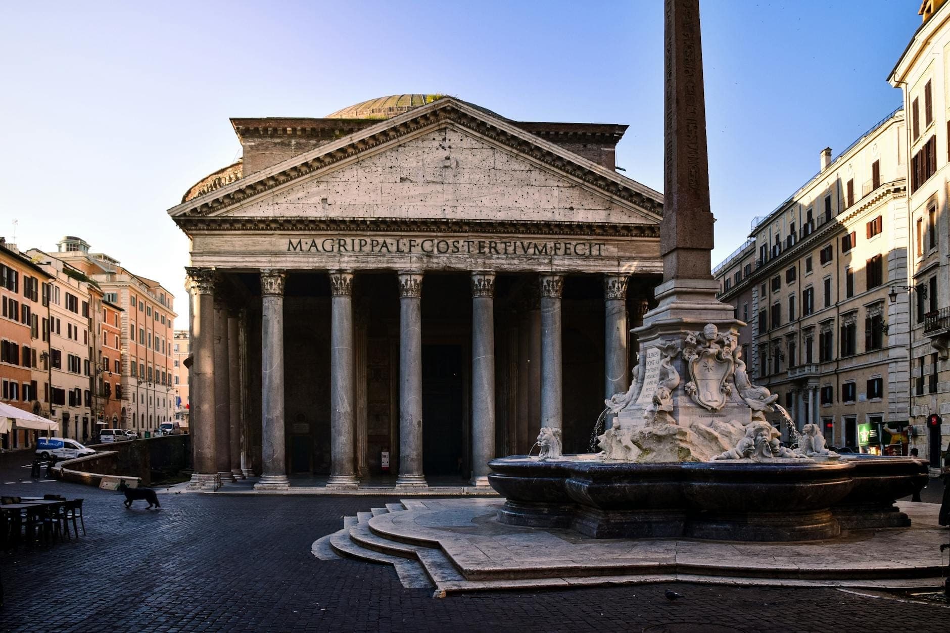 Vue large du Panthéon avec ses colonnes et sa fontaine devant, entouré de bâtiments dans le centre historique de Rome.