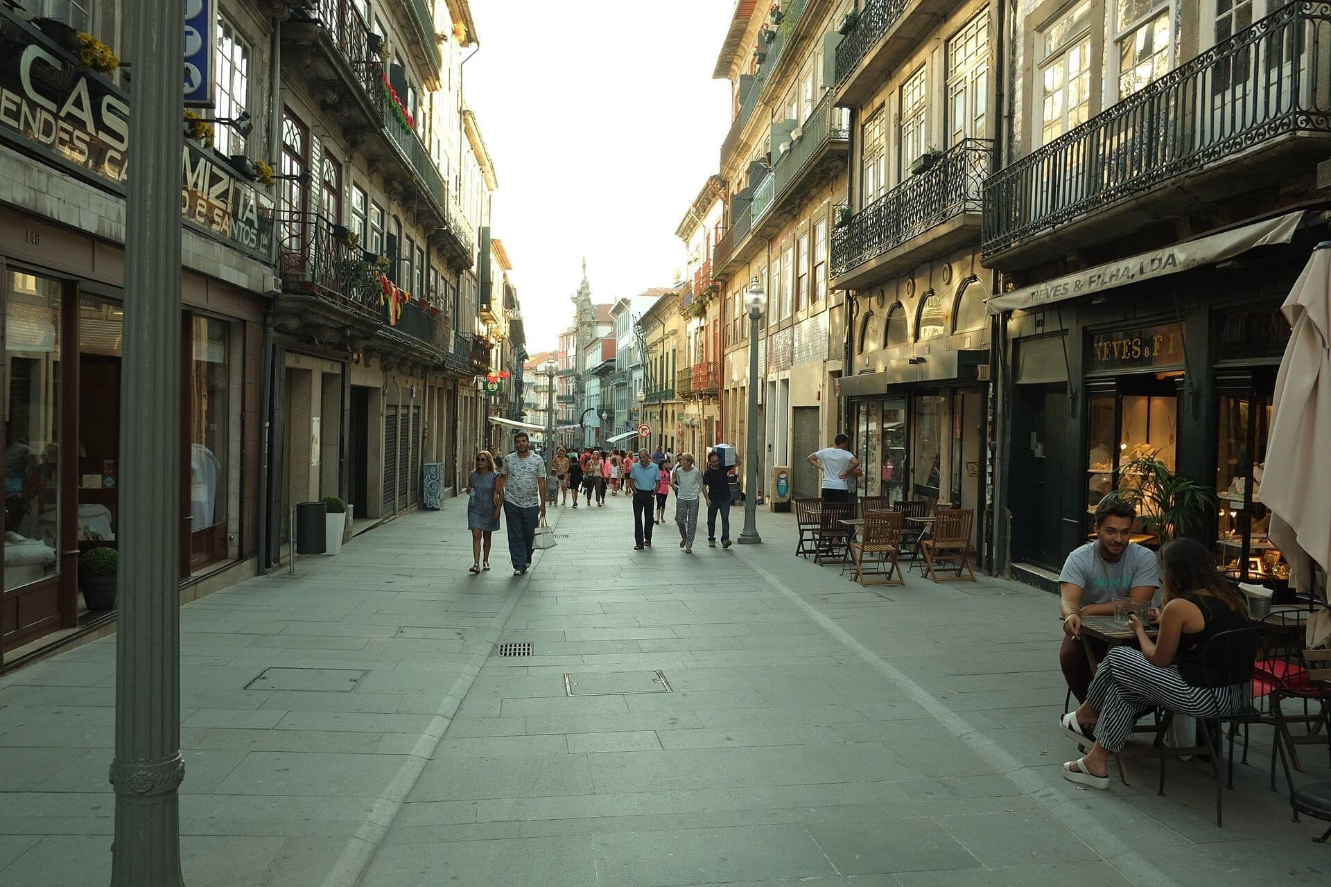 Fußgänger schlendern entlang der Rua das Flores in Porto, gesäumt von historischen Fassaden, schmiedeeisernen Balkonen und Straßencafés im warmen Abendlicht.