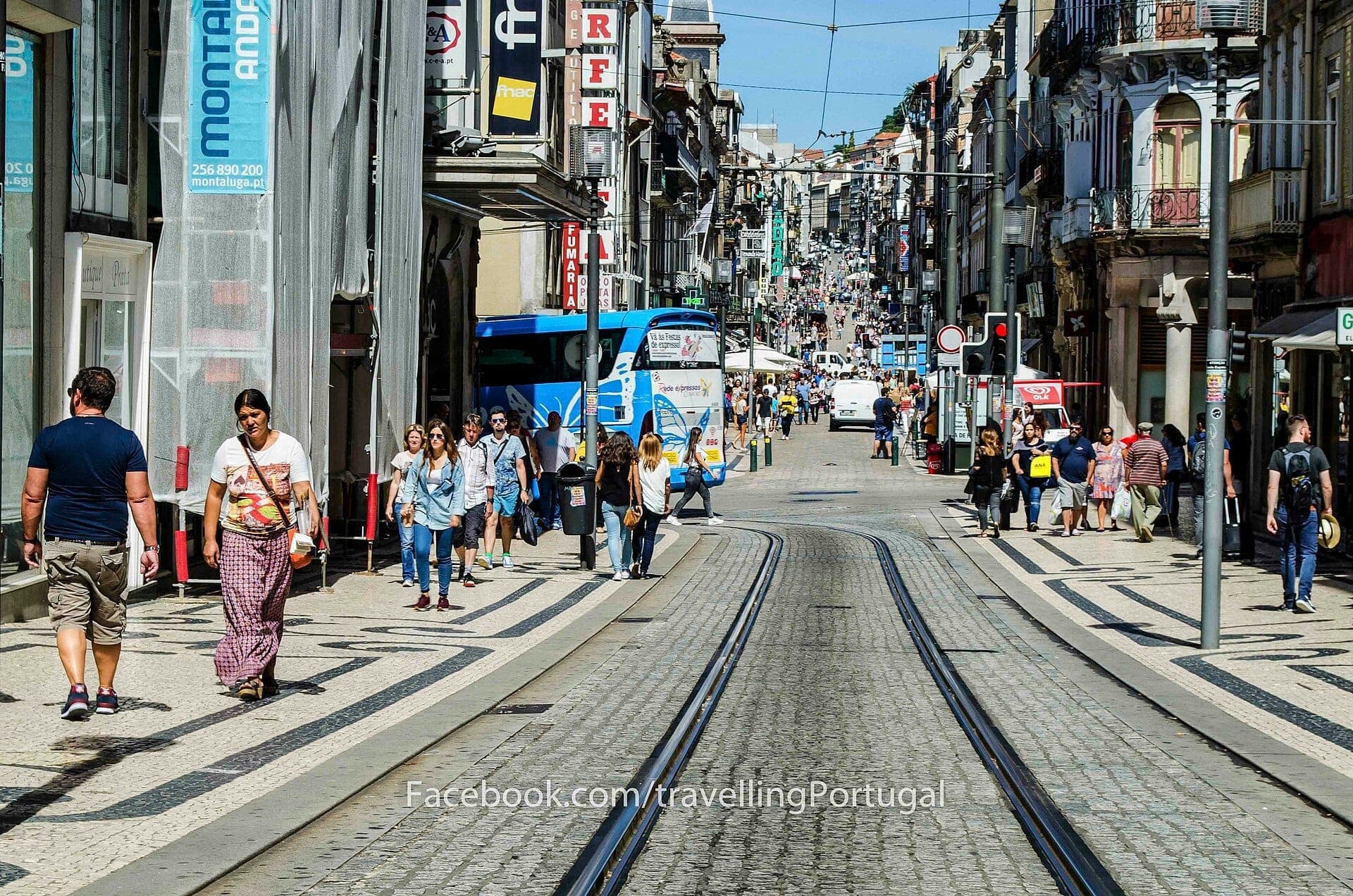 Rua de Santa Catarina w Porto w słoneczny dzień, z pieszymi spacerującymi wzdłuż sklepów, kawiarni i torów tramwajowych otoczonych historycznymi budynkami.