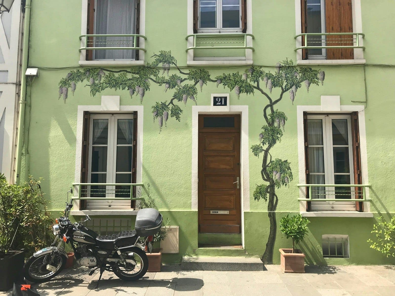 Pastel green townhouse with painted wisteria, wooden door, and motorbike parked outside on Rue Crémieux, Paris, under natural daylight.