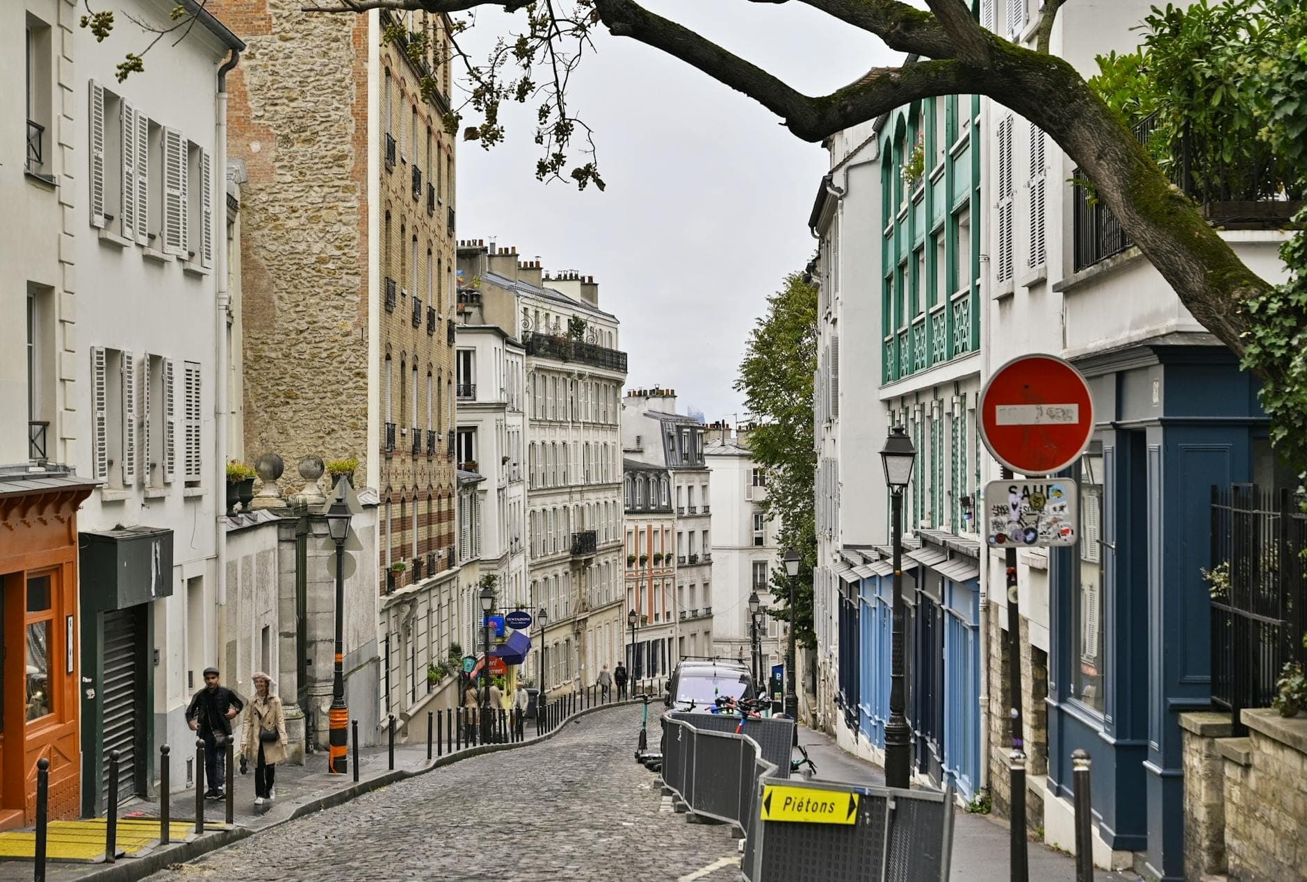 A gently curving, cobblestone street in Paris lined with classic buildings, small shops, and pedestrians, capturing the historic charm and daily life of Rue Mouffetard.