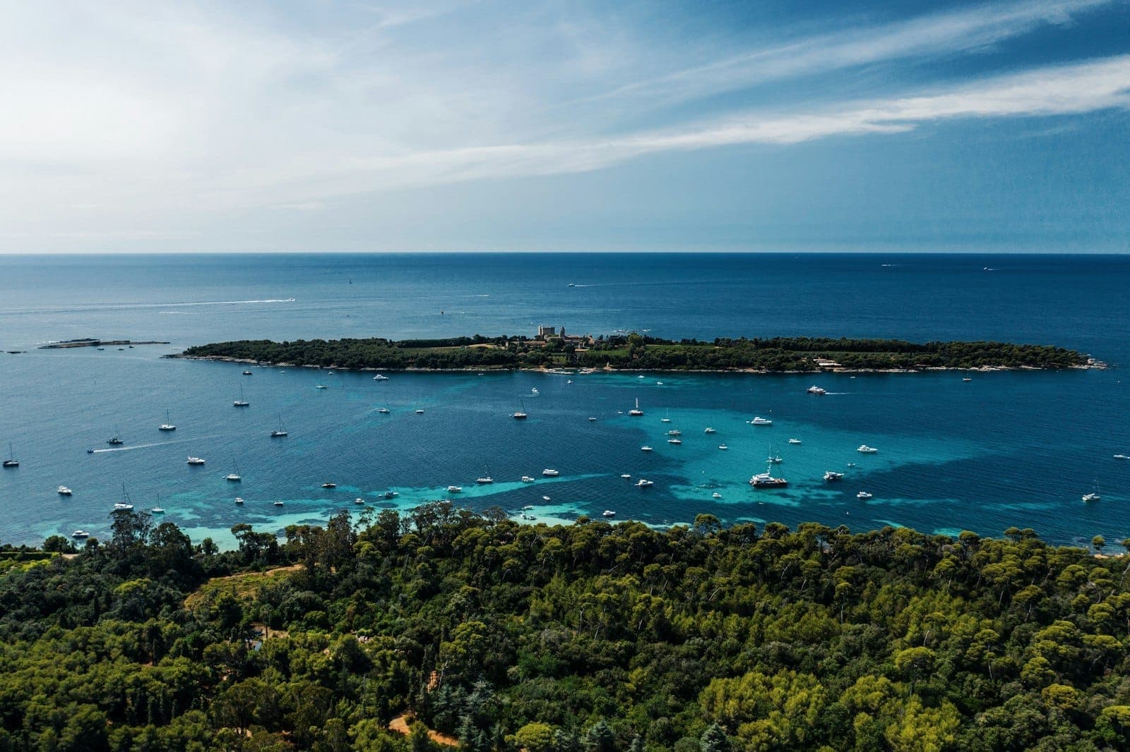 Вид с воздуха на Île Saint-Honorat в окружении бирюзовой воды и лодок — густая зелень и ясное голубое небо над головой.