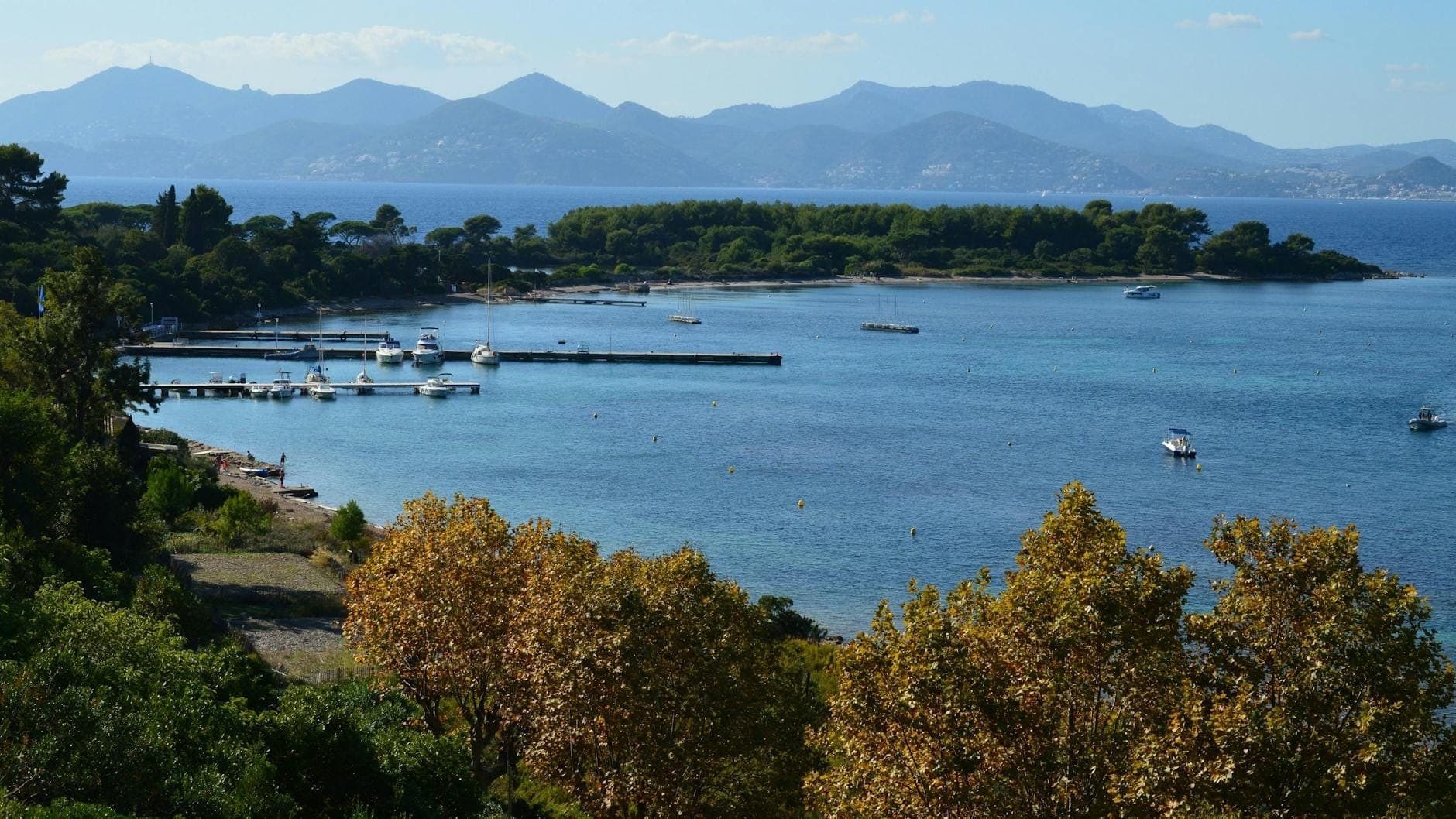 Вид на Île Sainte-Marguerite: сосны, прозрачная средиземноморская вода, небольшие лодки и горы вдали — природная красота и тишина острова рядом с Каннами.