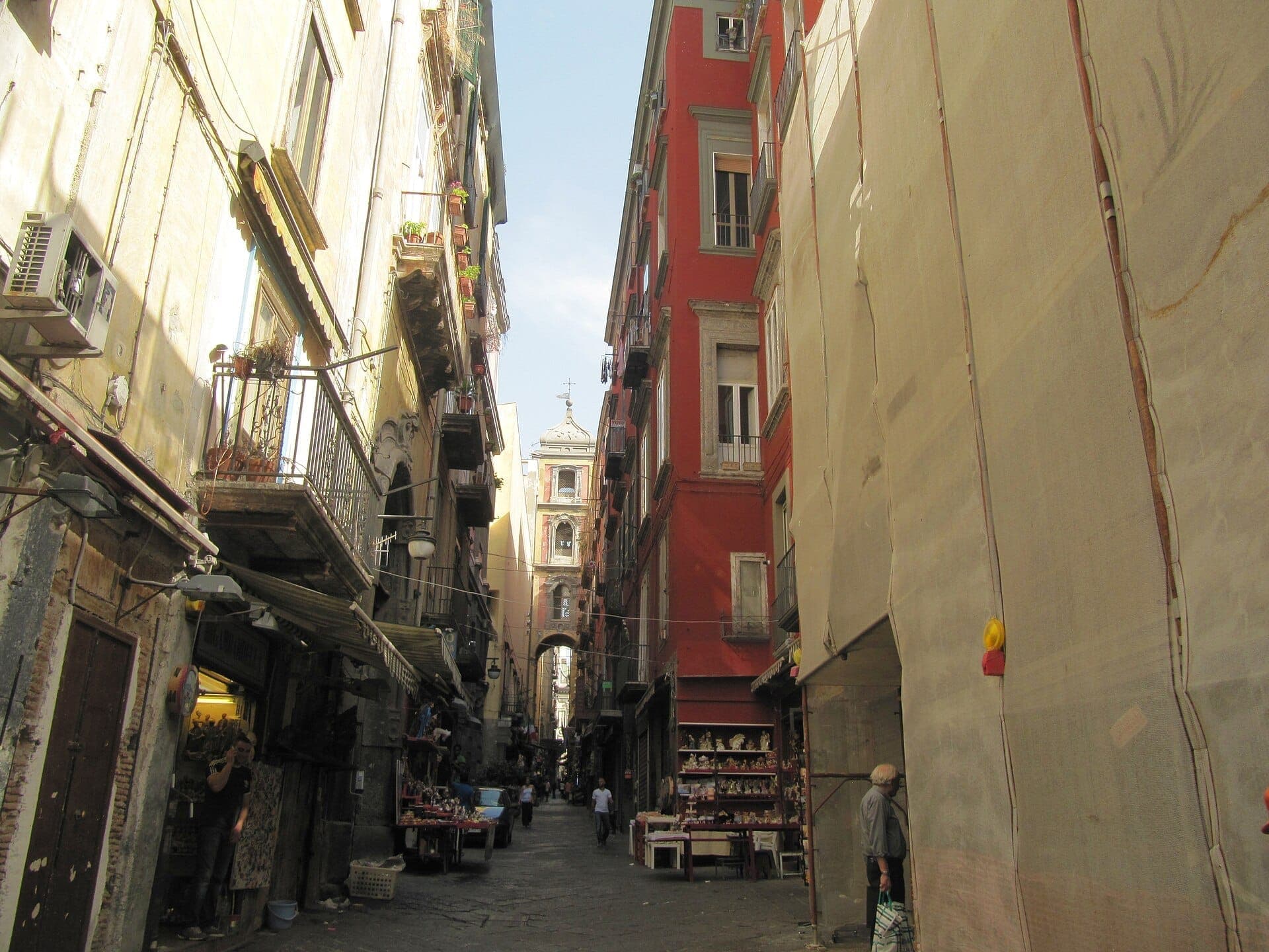 Rua estreita ladeada por prédios históricos e lojas de artesanato que vendem figuras de presépio na Via San Gregorio Armeno, em Nápoles.