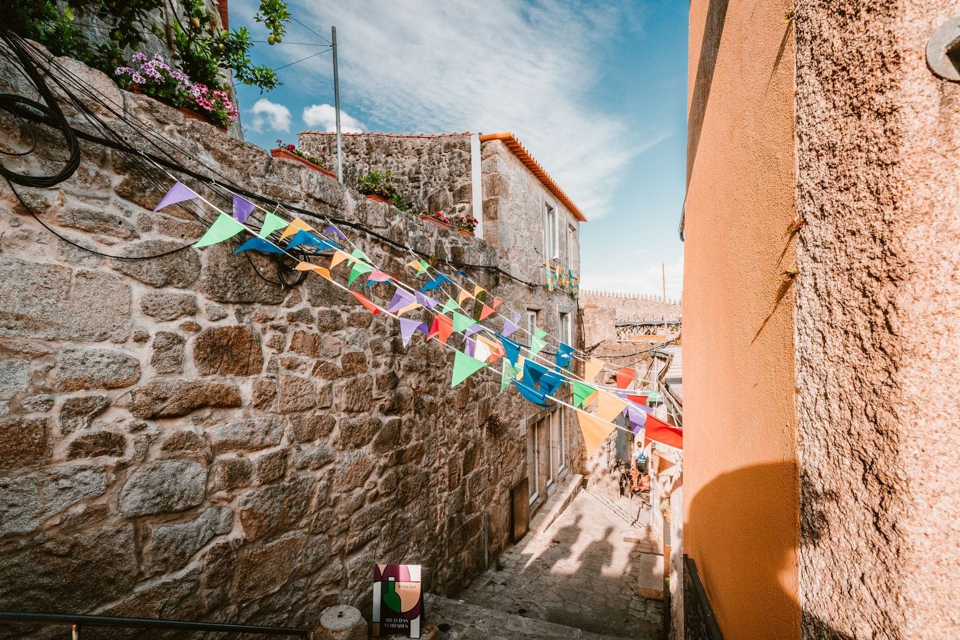 Calle estrecha de piedra en Oporto decorada con banderines coloridos de festival bajo un cielo azul brillante, capturando el ambiente festivo de São João.