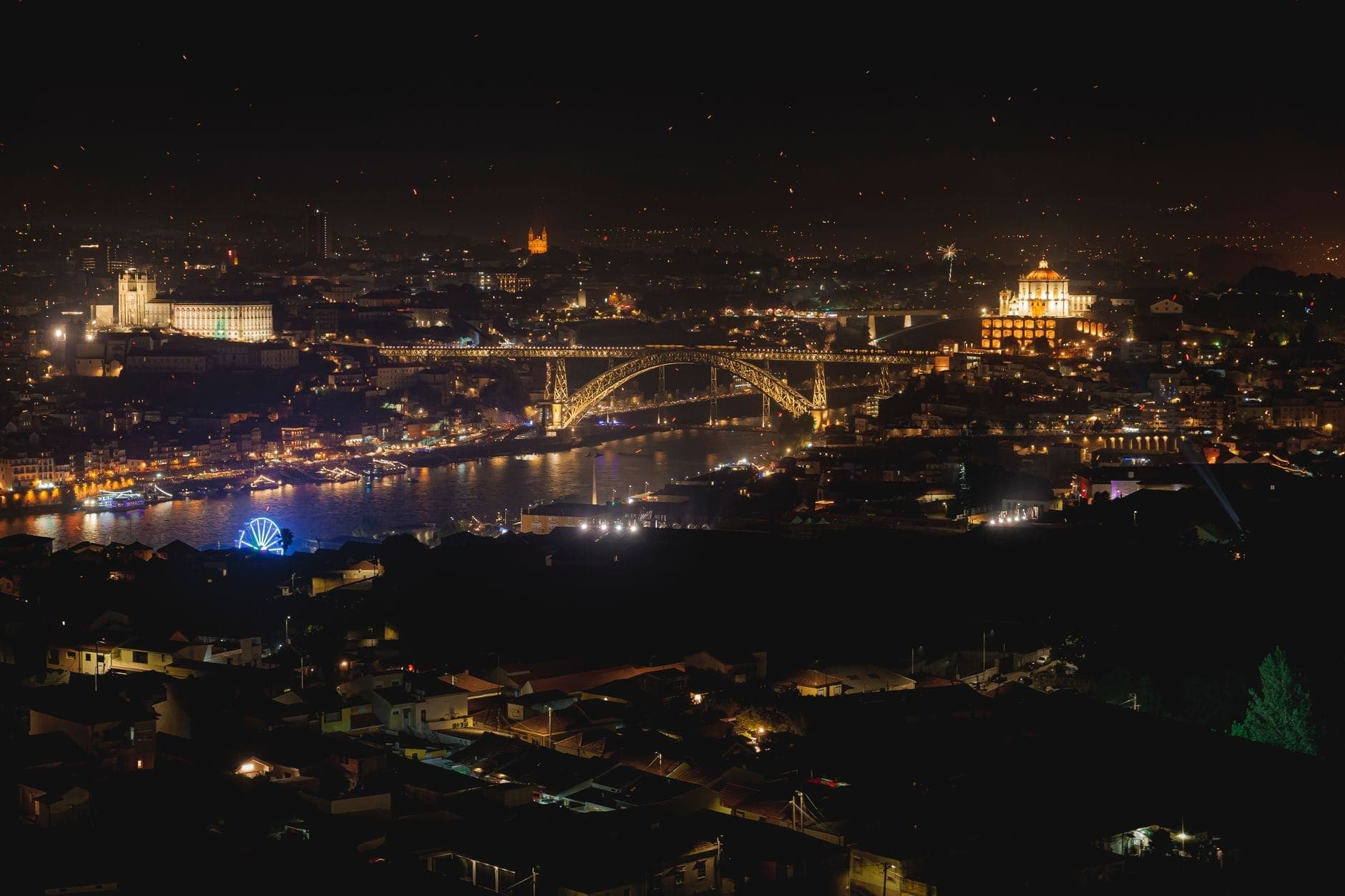Vista nocturna de Porto con el iluminado Puente Dom Luís I sobre el río Douro y las luces de la ciudad, mostrando lugares populares de festivales.