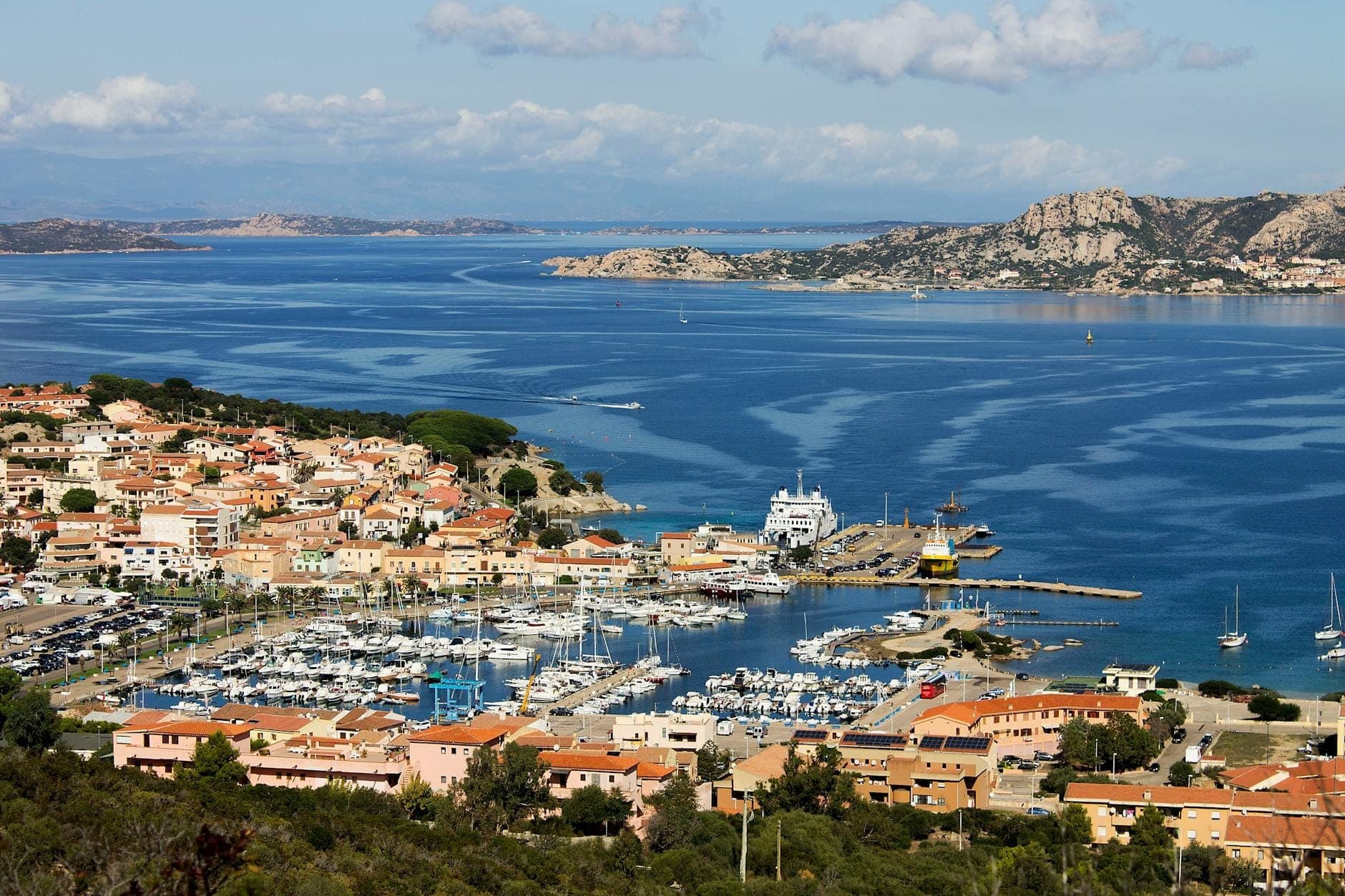 Luftaufnahme eines Yachthafens mit Jachten und Booten, einer Küstenstadt und felsigen Inseln in der Region Costa Smeralda auf Sardinien.