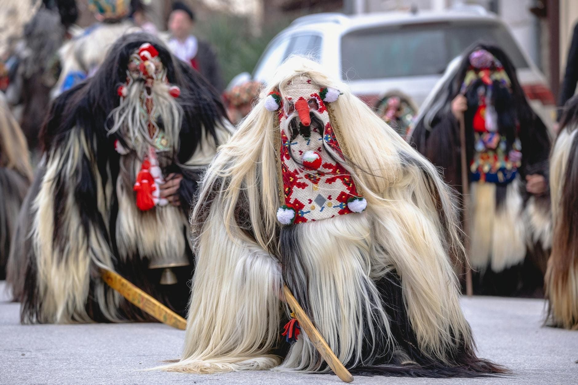 Menschen in traditionellen sardischen Mamuthones-Kostümen mit zotteligen schwarz-weißen Schaffellen und Holzmasken bei einem Straßenfest.