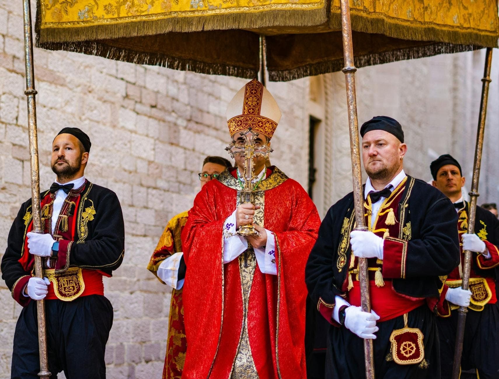 Eine traditionelle religiöse Prozession mit Männern in prachtvollen Kostümen und einem Bischof unter einem Baldachin, vermutlich während eines sardischen Sommerfestivals.