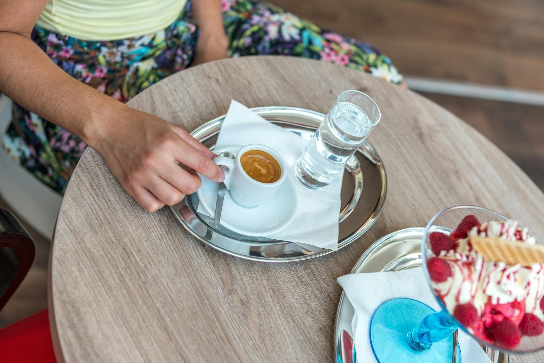 Una persona en una mesa de café sosteniendo un espresso con un vaso de agua y un postre, evocando la cultura de los cafés italianos.
