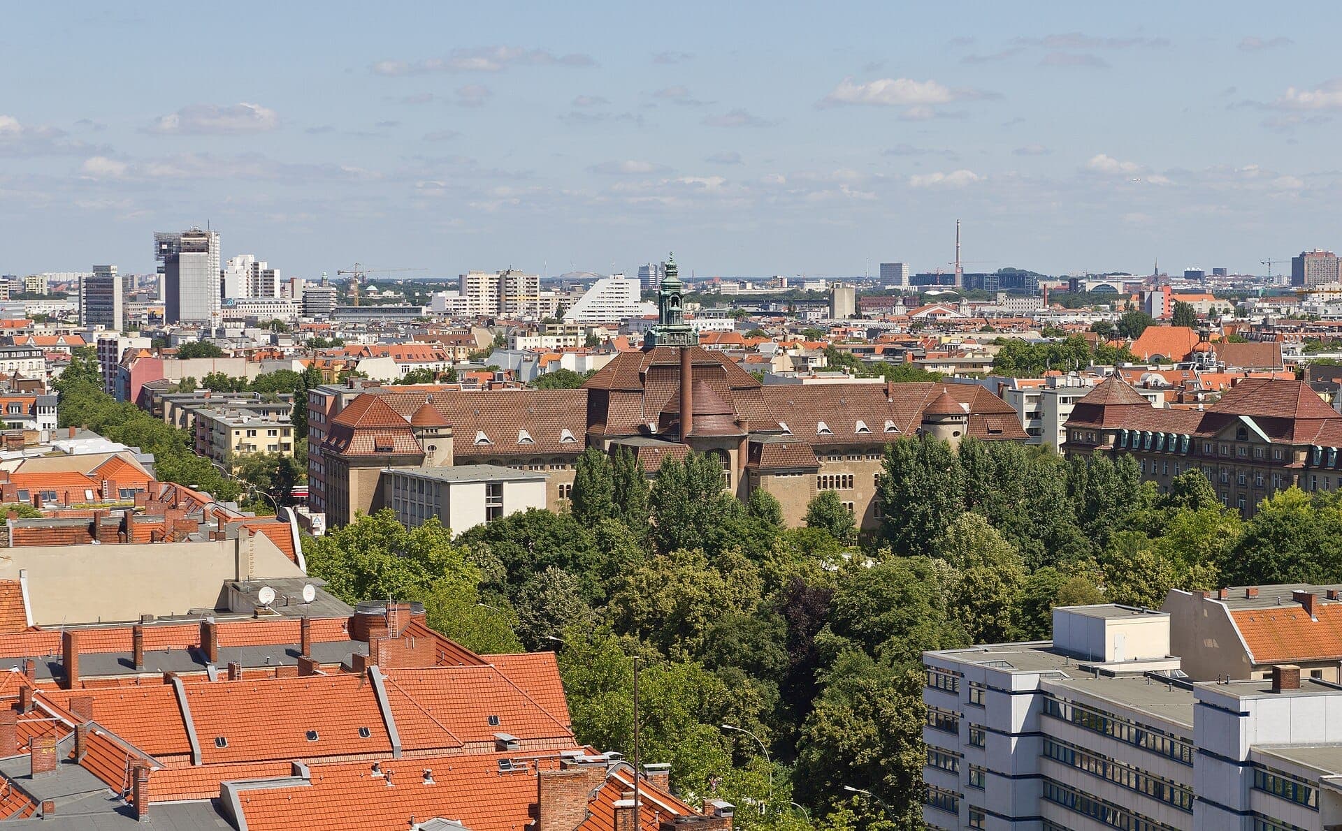 มุมมองทางอากาศของ Schöneberg ในกรุง Berlin โดดเด่นด้วยอาคารหลังคาสีแดง ต้นไม้เขียวชอุ่ม และศาลาว่าการเมืองประวัติศาสตร์ใต้ท้องฟ้าสีฟ้า