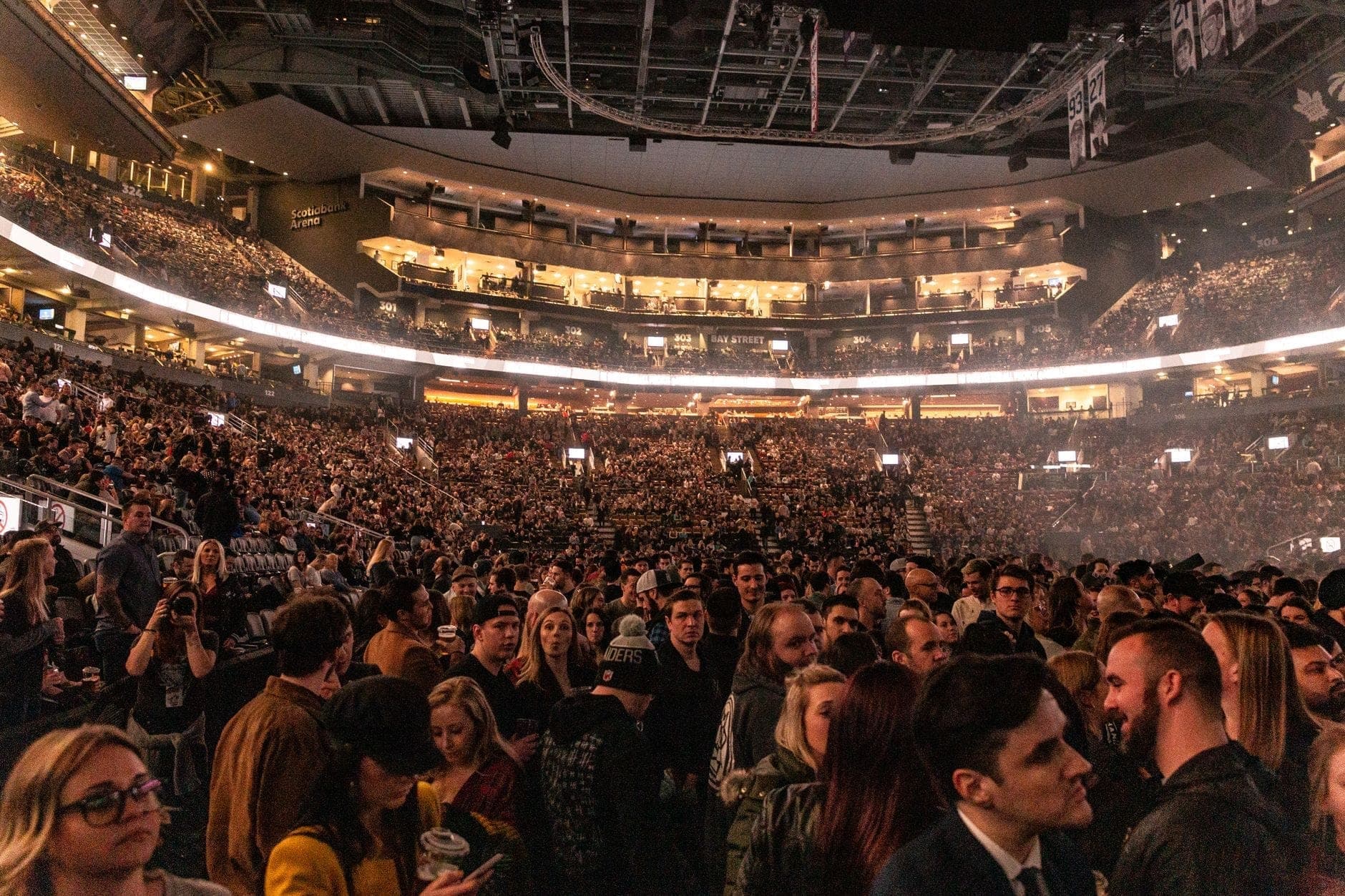 Una grande folla all'interno di un'arena moderna, con luci brillanti che illuminano i settori gremiti di tifosi entusiasti, evocando l'atmosfera vibrante di un evento dal vivo.