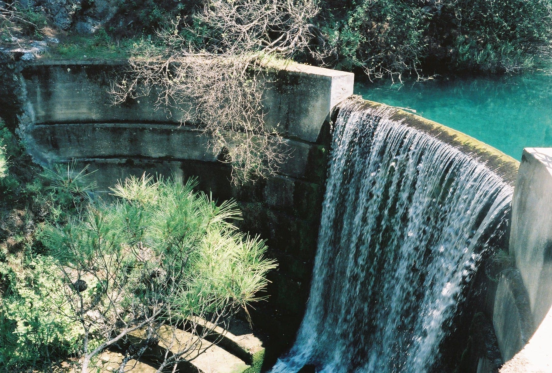 Barrage en béton avec cascade et eau turquoise à Seven Springs, entouré d'une végétation luxuriante et de soleil dans l'oasis intérieure de Rhodes.