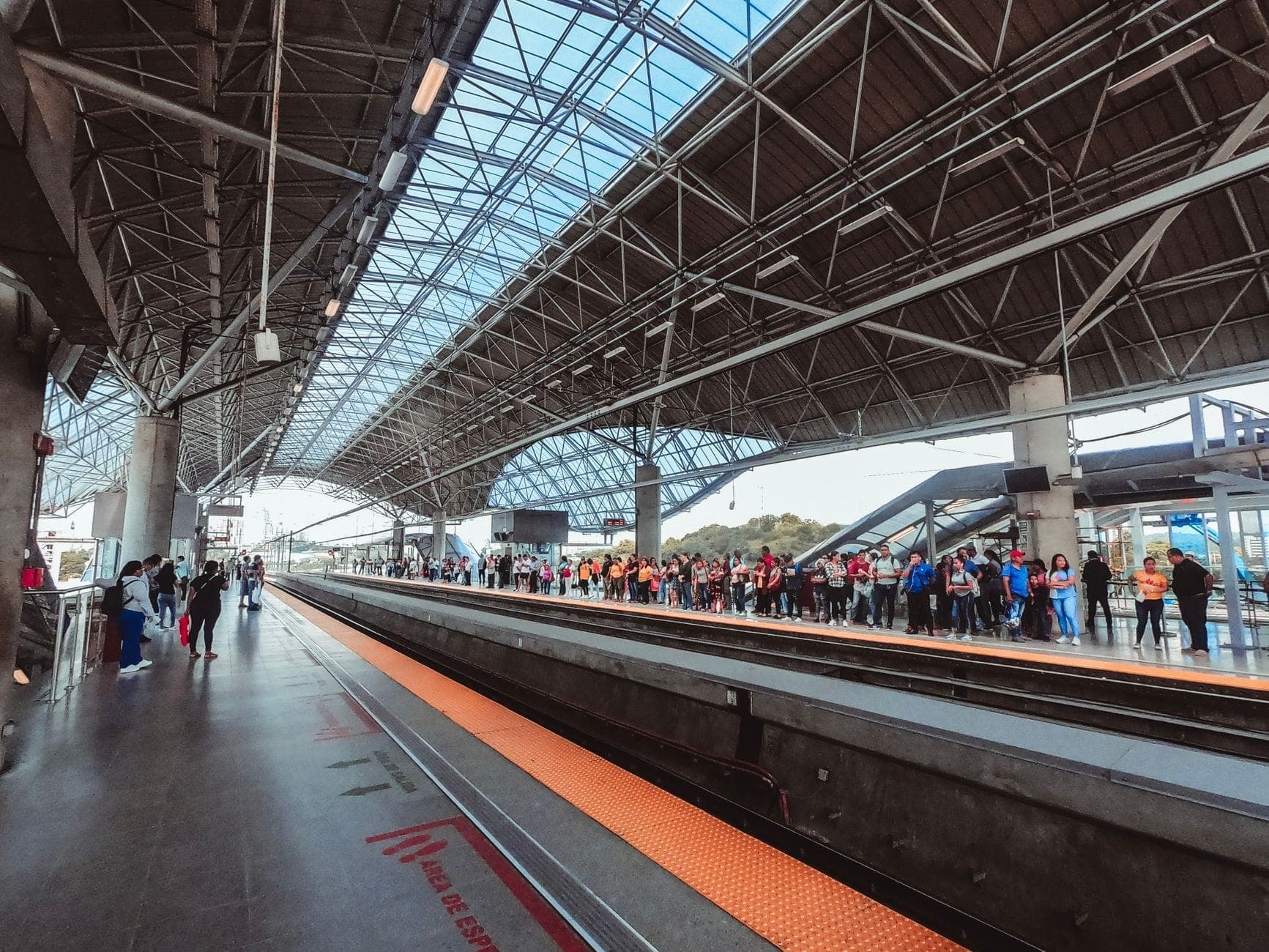 สถานีรถไฟใต้ดินที่ทันสมัยและกว้างขวางพร้อมหลังคากระจก ผู้คนรอบนชานชาลา และแสงธรรมชาติที่สดใสอันเป็นเอกลักษณ์ของระบบขนส่งสาธารณะของ Guadalajara