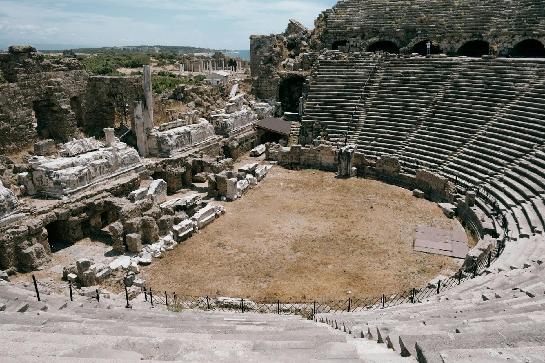 Weitwinkelaufnahme der steinernen Sitzreihen des antiken Theaters von Side mit den teilweise erhaltenen Bühnenruinen unter hellem Himmel – ideal als Hero-Bild für einen Reiseguide.
