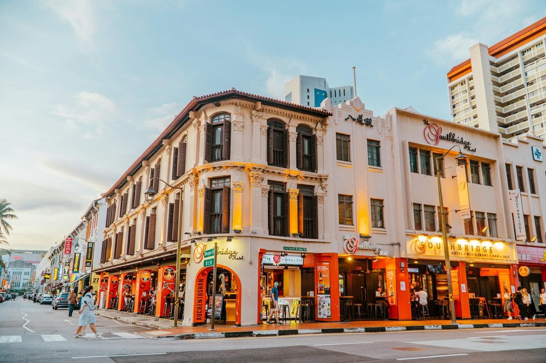 ถนนที่คึกคักในสิงคโปร์ยามพลบค่ำ เรียงรายด้วยชอปเฮาส์ทางประวัติศาสตร์และหน้าร้านอาหารที่ส่องสว่าง สะท้อนให้เห็นย่านที่ขึ้นชื่อเรื่องความหลากหลายของตัวเลือกร้านอาหาร