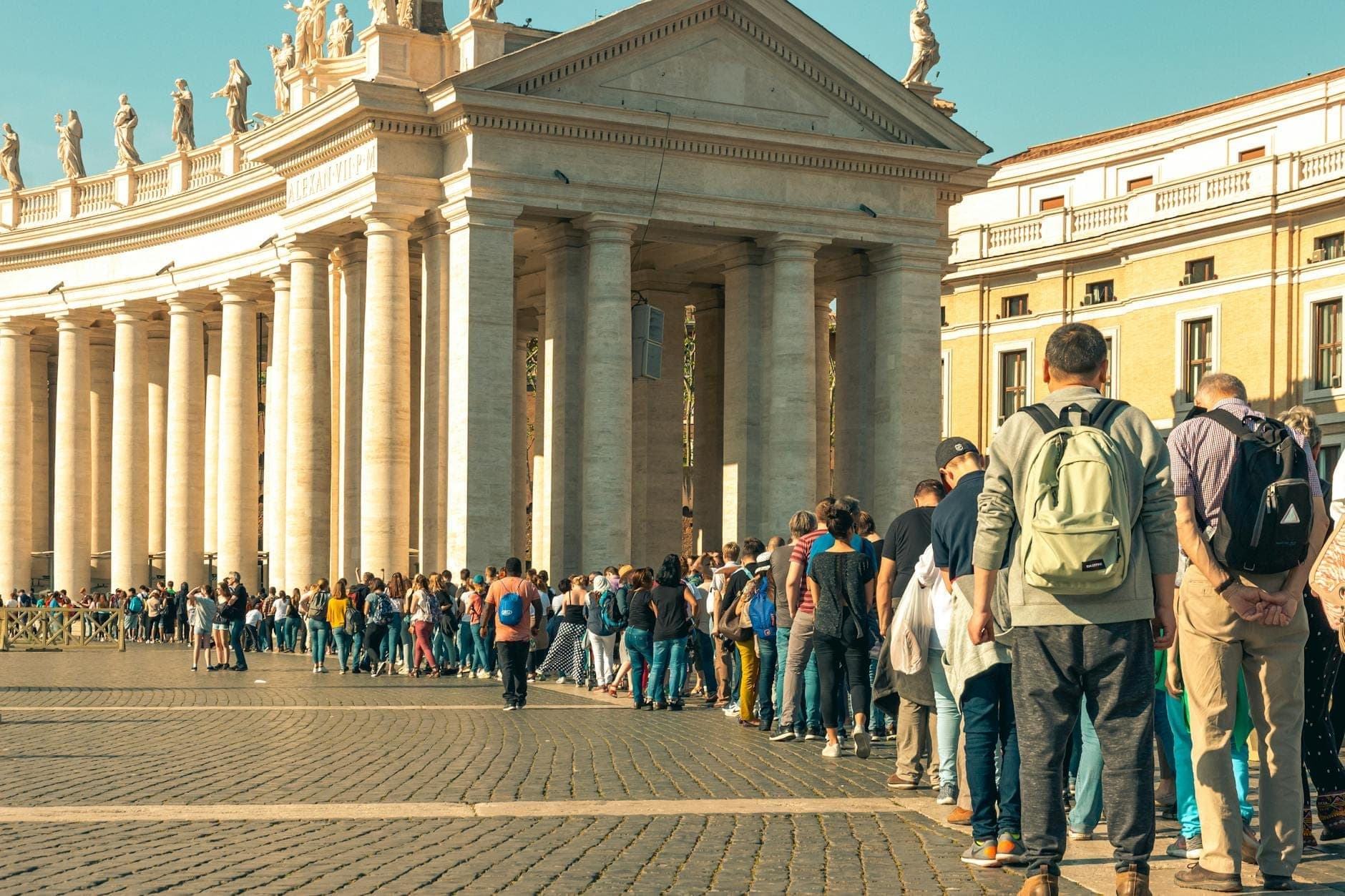 Mahabang linya ng mga turista na naghihintay sa labas ng isang magandang gusaling may mga haligi sa ilalim ng maliwanag na langit, na nagpapakita ng matagal na pila sa mga pangunahing atraksyon ng Roma.