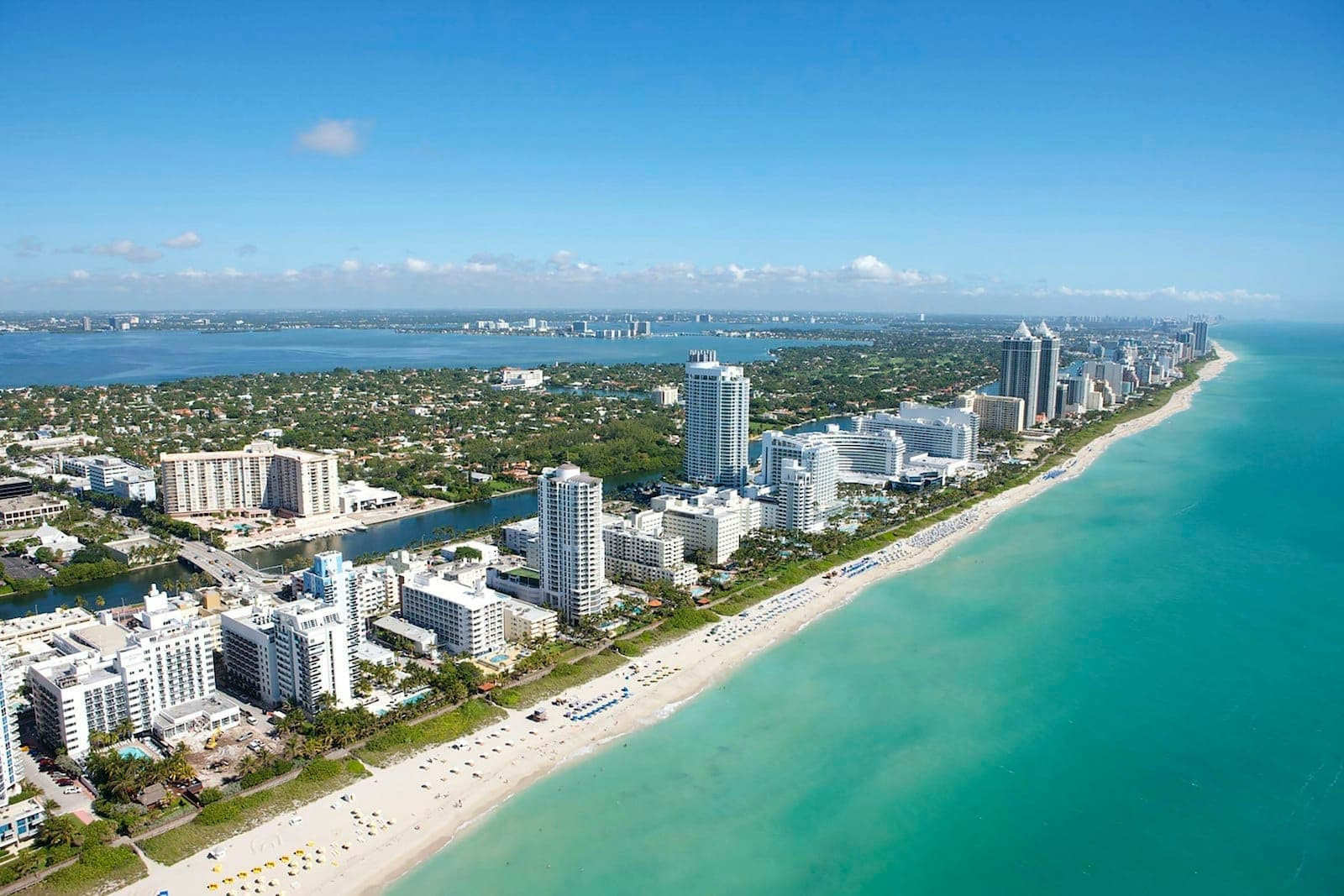 Aerial view of South Beach showing white sand, turquoise water, and a stretch of Art Deco hotels and high-rise buildings along the coast.