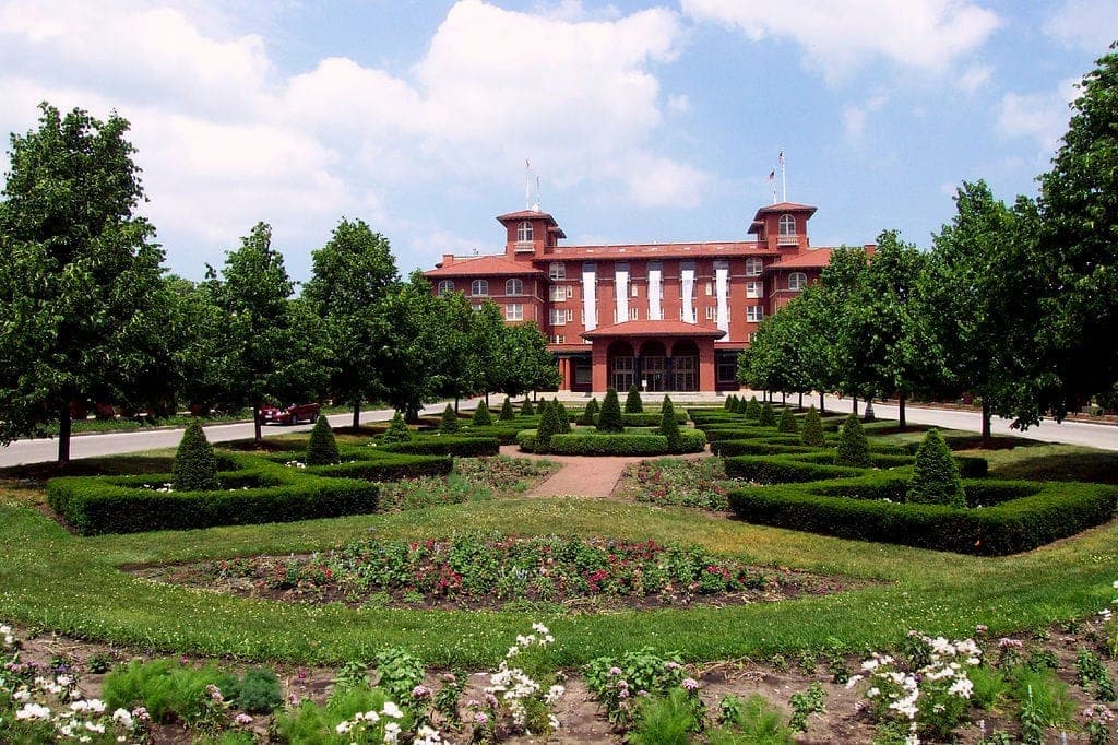 Centro Cultural South Shore de ladrillo rojo con jardín simétrico, setos cuidados y frondosos árboles verdes bajo un cielo azul brillante.