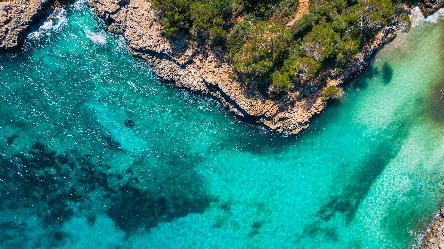 Luftaufnahme einer felsigen Küste mit türkisfarbenem Wasser und üppigem Grün, das die Naturschönheit und das klare Meer des südöstlichen Mallorcas zeigt.