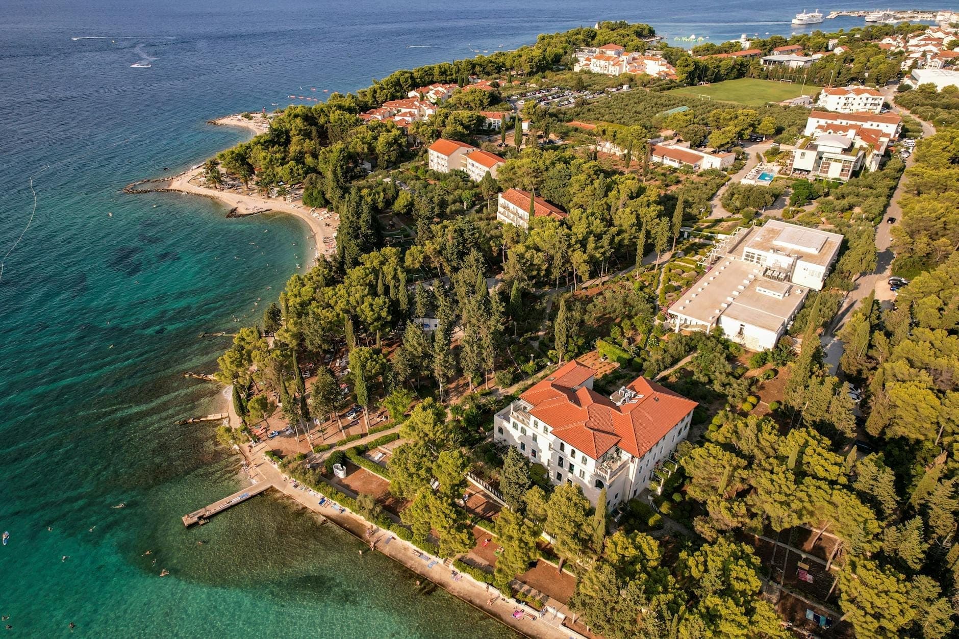 Vista aerea della costa di Spalato in estate con alberi verdi, spiagge, mare blu cristallino ed edifici illuminati dal sole vicino alla riva.