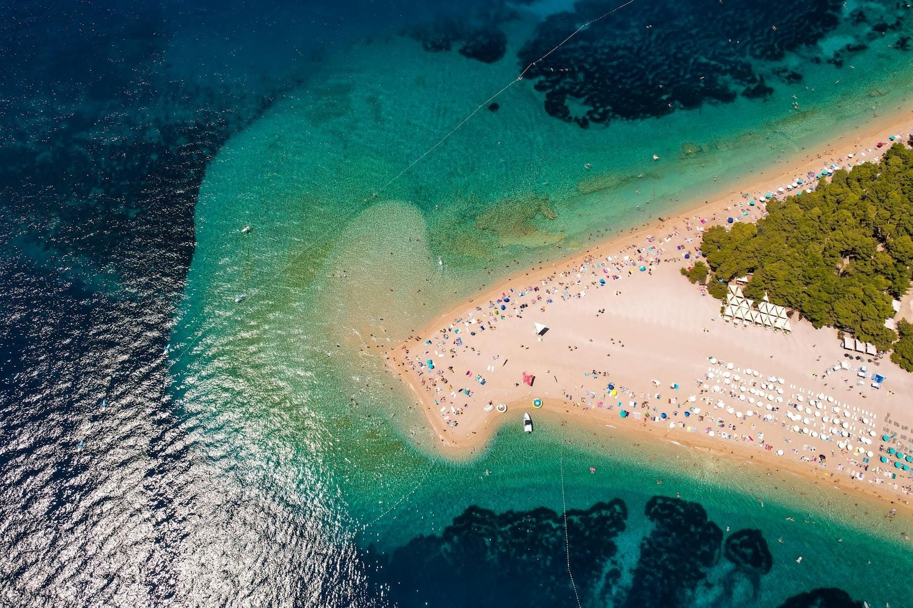Vue aérienne d'une plage croate bondée avec des parasols, des bains de soleil et des nageurs par une ensoleillée journée d'été.