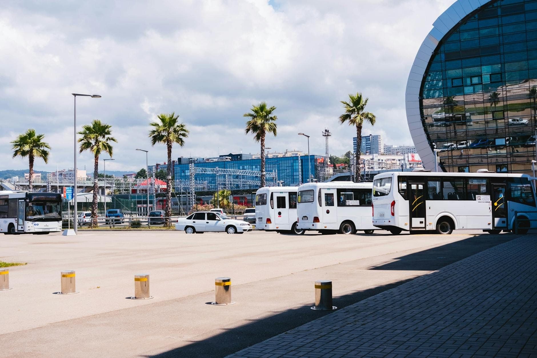 Stazione degli autobus moderna con autobus bianchi, palme e un edificio contemporaneo in vetro, probabilmente in una città mediterranea come Spalato.