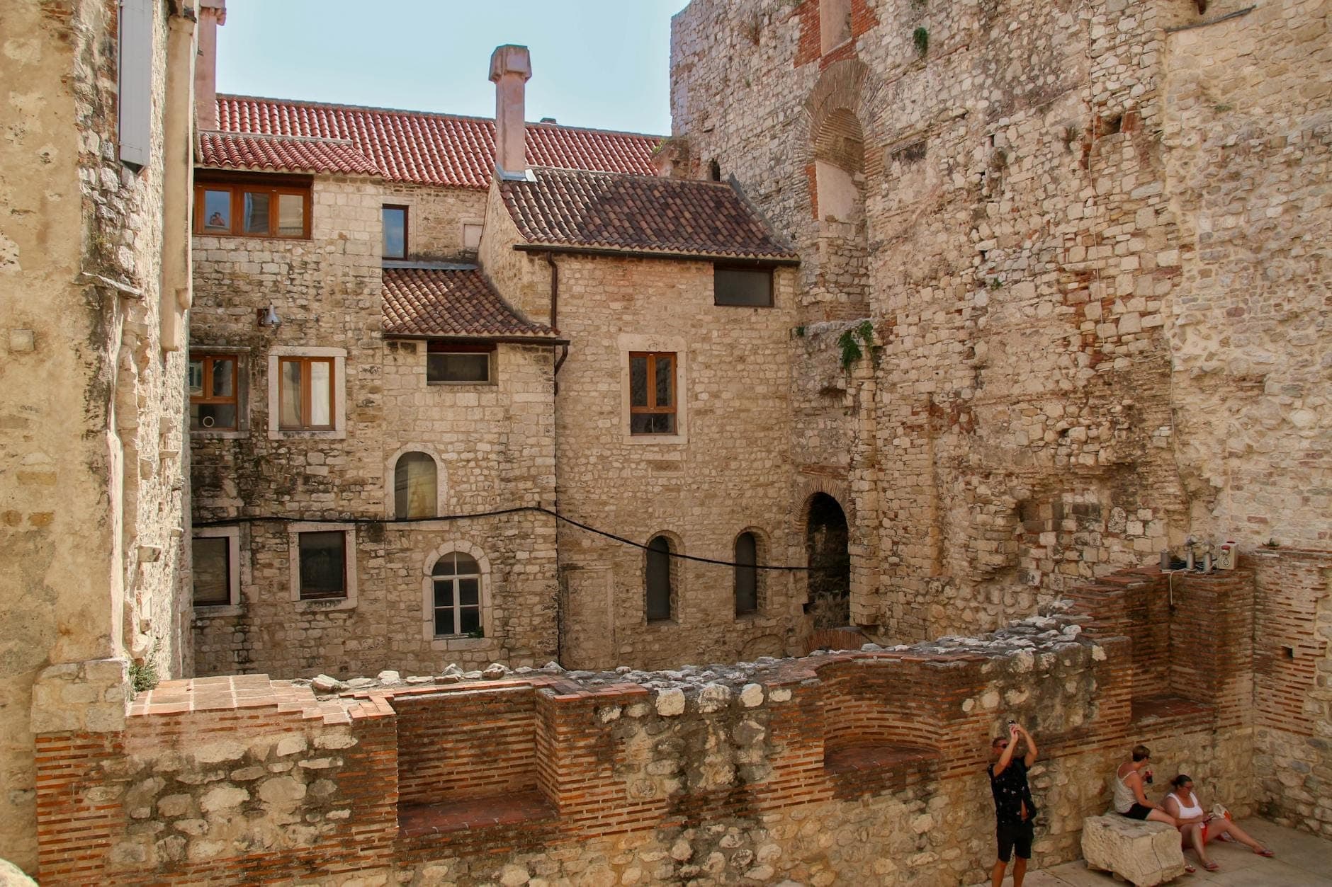 Edifici residenziali in pietra integrati nelle antiche mura del palazzo con persone sedute tra le rovine nella città vecchia di Spalato.