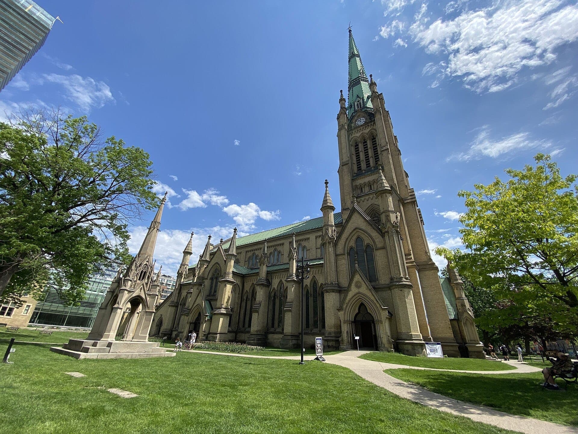 Cattedrale di St. James nel centro di Toronto, con la sua alta guglia in stile Neogotico, circondata da prati verdi e cielo azzurro in una giornata di sole.