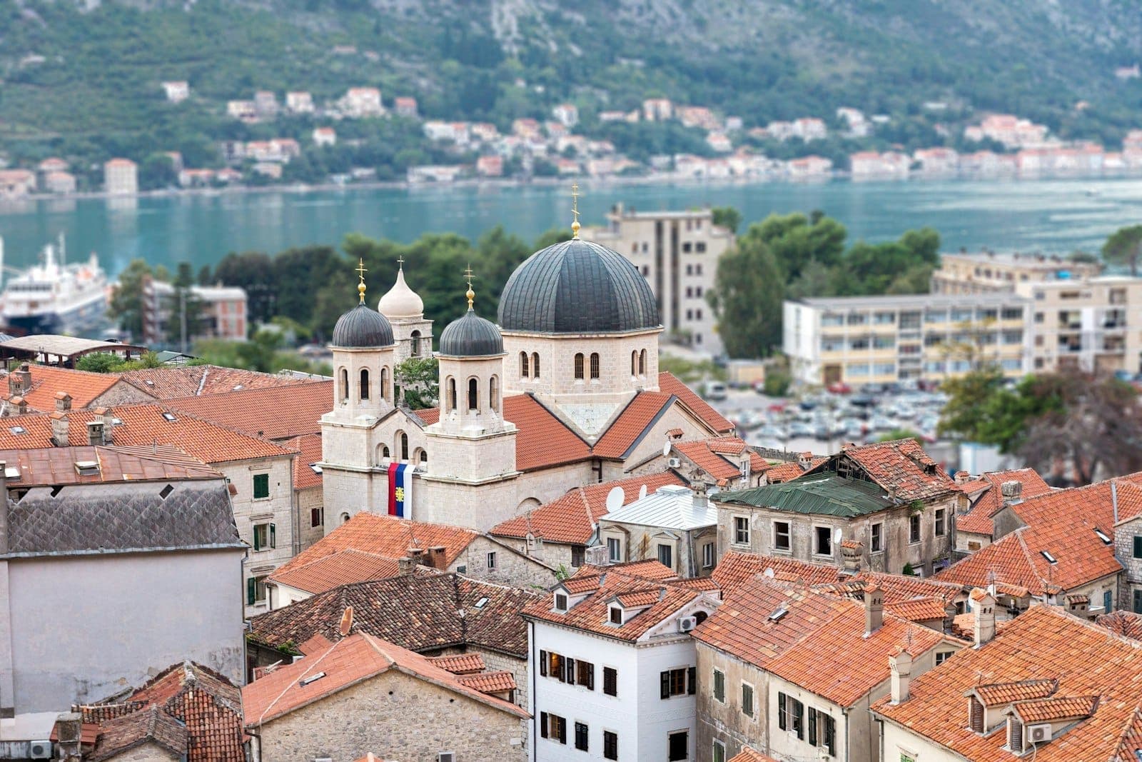 Église Saint-Nicolas dans la vieille ville de Kotor avec ses dômes noirs distinctifs et ses tours jumelles, entourée de toits en tuiles rouges et surplombant la baie.