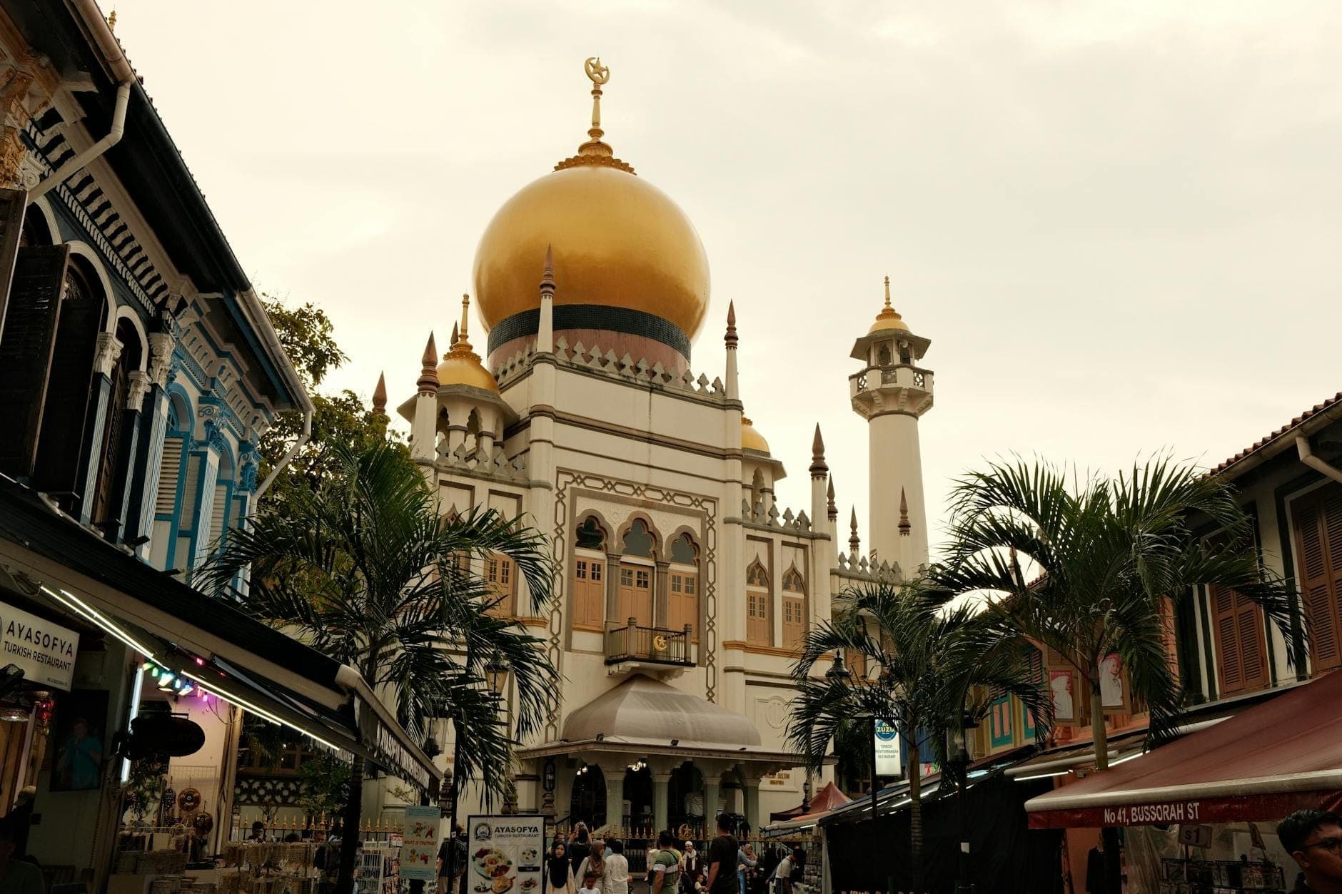 Sultan Mosque framed by palm trees and shophouses at dusk, with its iconic golden dome illuminated in the heart of Kampong Glam.