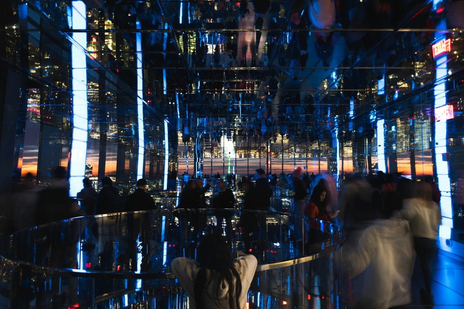 ผู้เข้าชมกำลังเดินชมงานศิลปะกระจกเงาสุดล้ำยามพระอาทิตย์ตกใน SUMMIT One Vanderbilt พร้อมวิวเมืองและเงาสะท้อนที่เพิ่มบรรยากาศแห่งอนาคตให้กับหอชมวิวนี้