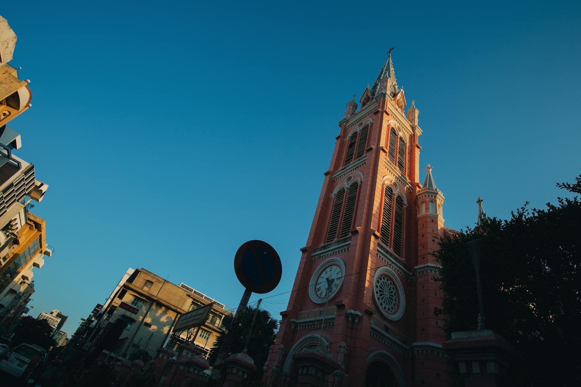 หอระฆังสีชมพูสไตล์กอธิค-โรมาเนสก์ของวัดตันดิ่nhตั้งตระหง่านสู่ท้องฟ้าสีครามในนครโฮจิมินห์ ล้อมรอบด้วยตึกรามและแมกไม้