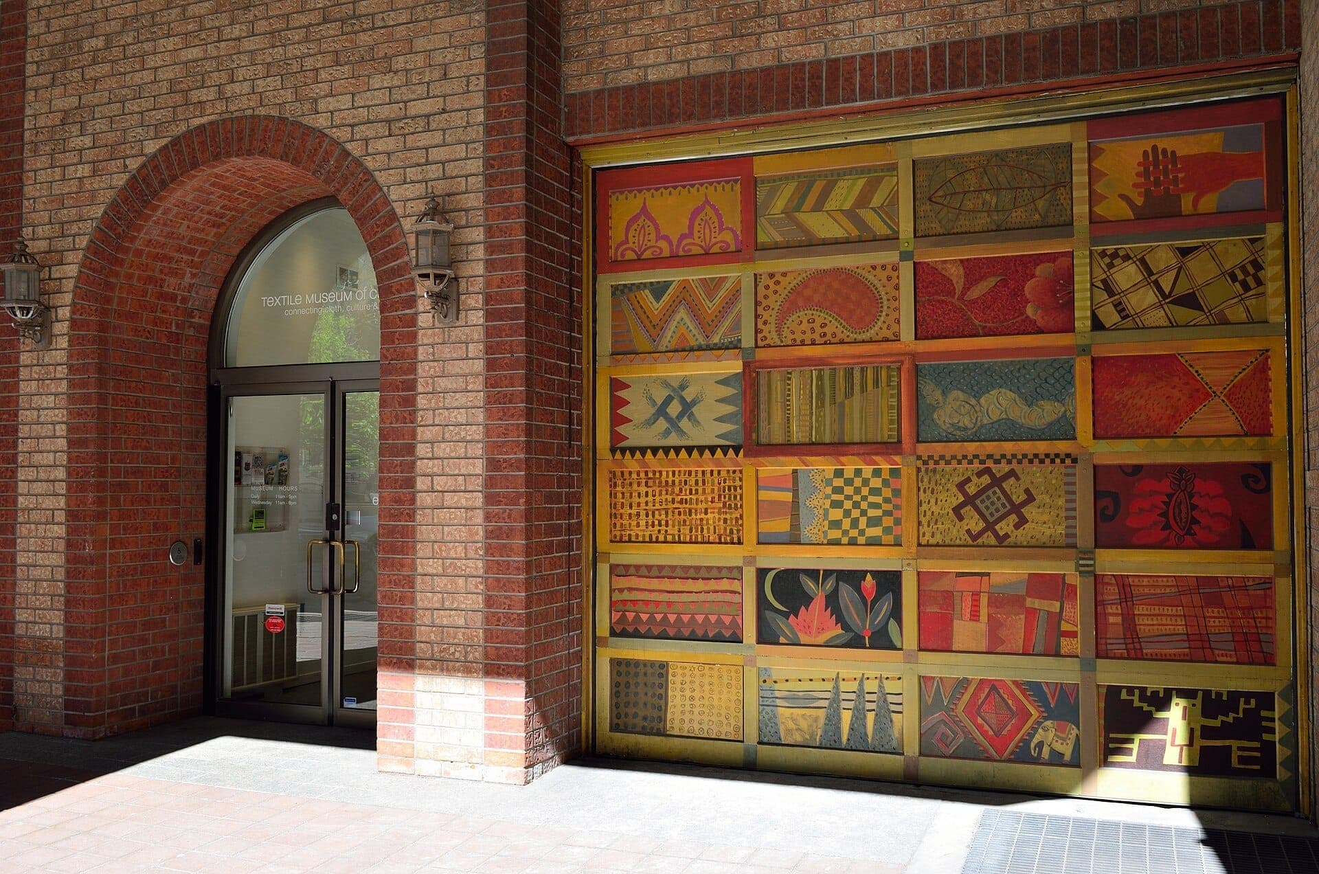 Ingresso al Textile Museum of Canada con un grande murale colorato a motivi e una porta in vetro inserita in un arco di mattoni.