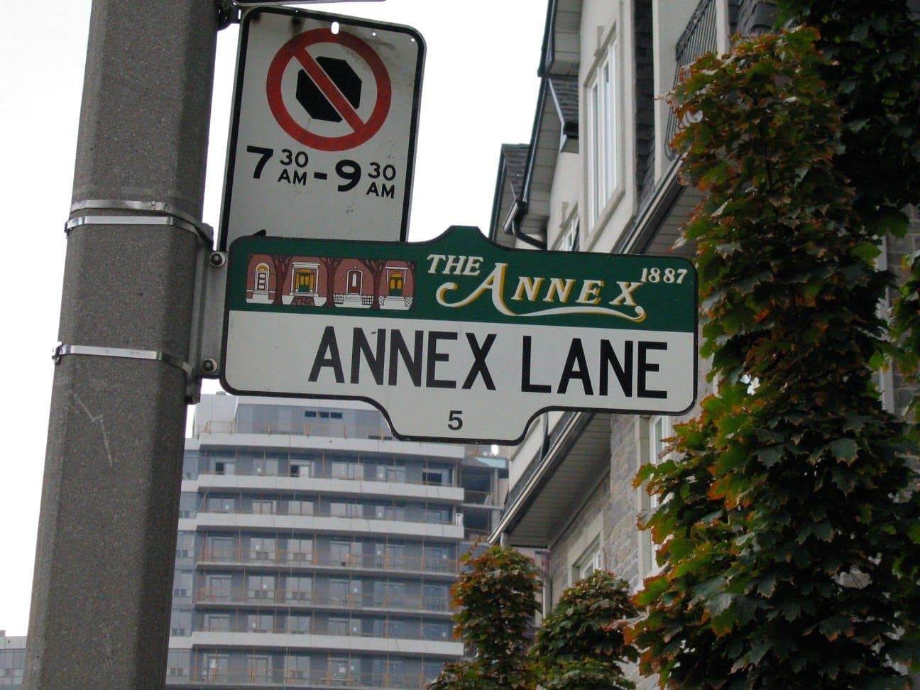 Primo piano di un cartello stradale per Annex Lane nel quartiere The Annex, Toronto, con appartamenti, alberi verdi ed edifici moderni sullo sfondo.