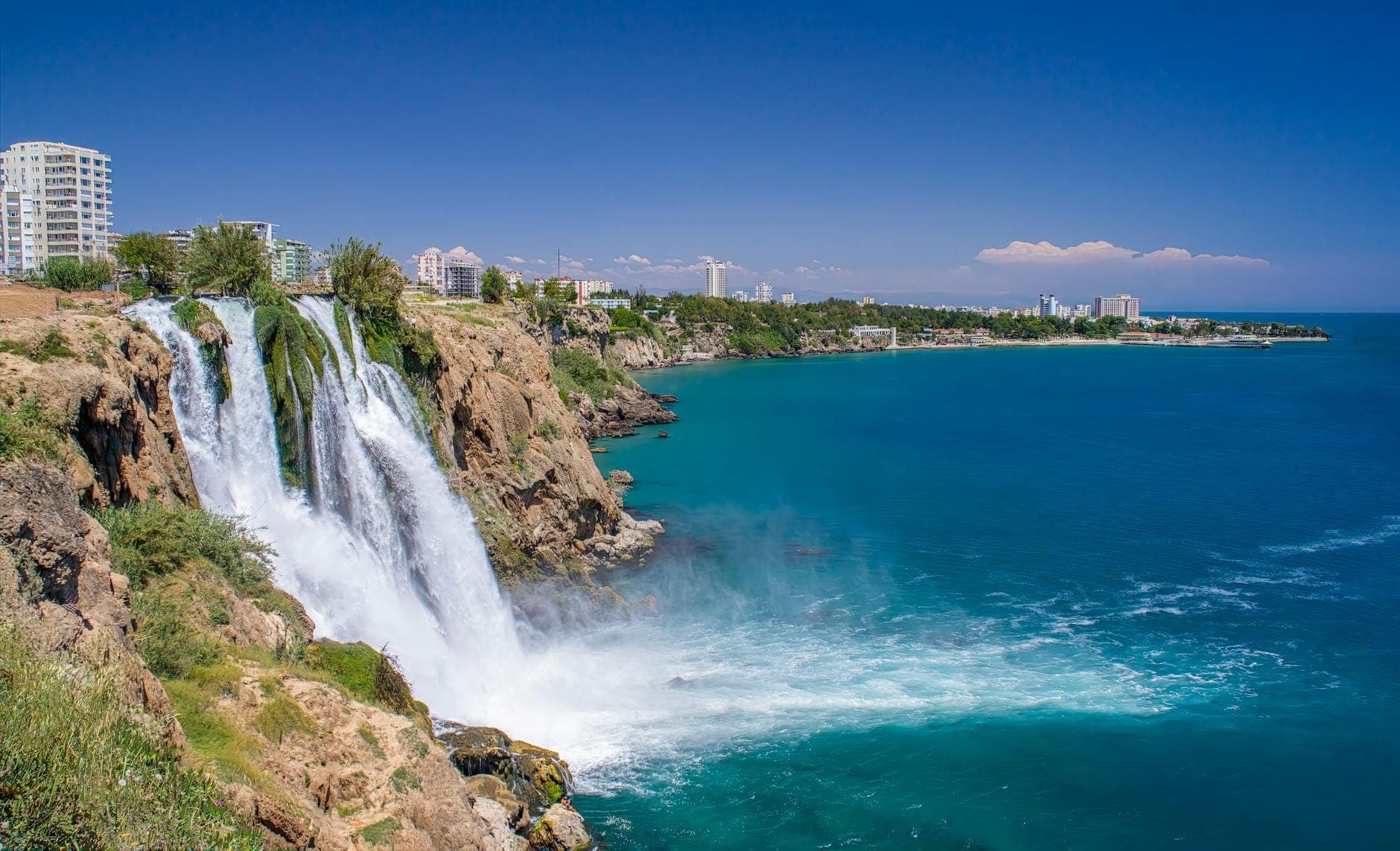Les cascades de Düden se déversant des falaises dans la mer Méditerranée avec les bâtiments et le littoral d'Antalya en arrière-plan.