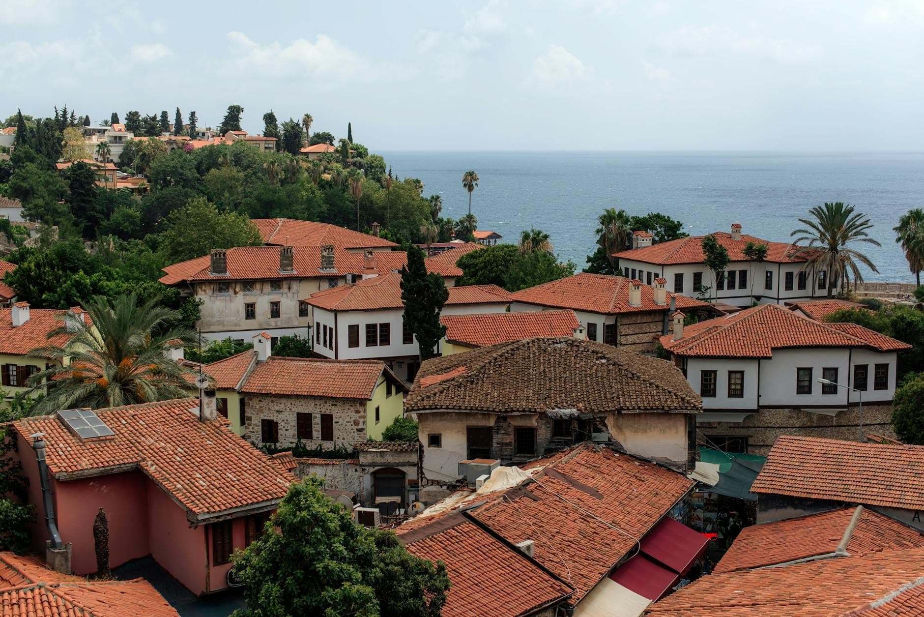 Vue sur les toits de tuiles rouges et les maisons historiques du vieux quartier de Antalya, Kaleiçi, avec une végétation luxuriante et la mer Méditerranée en arrière-plan.